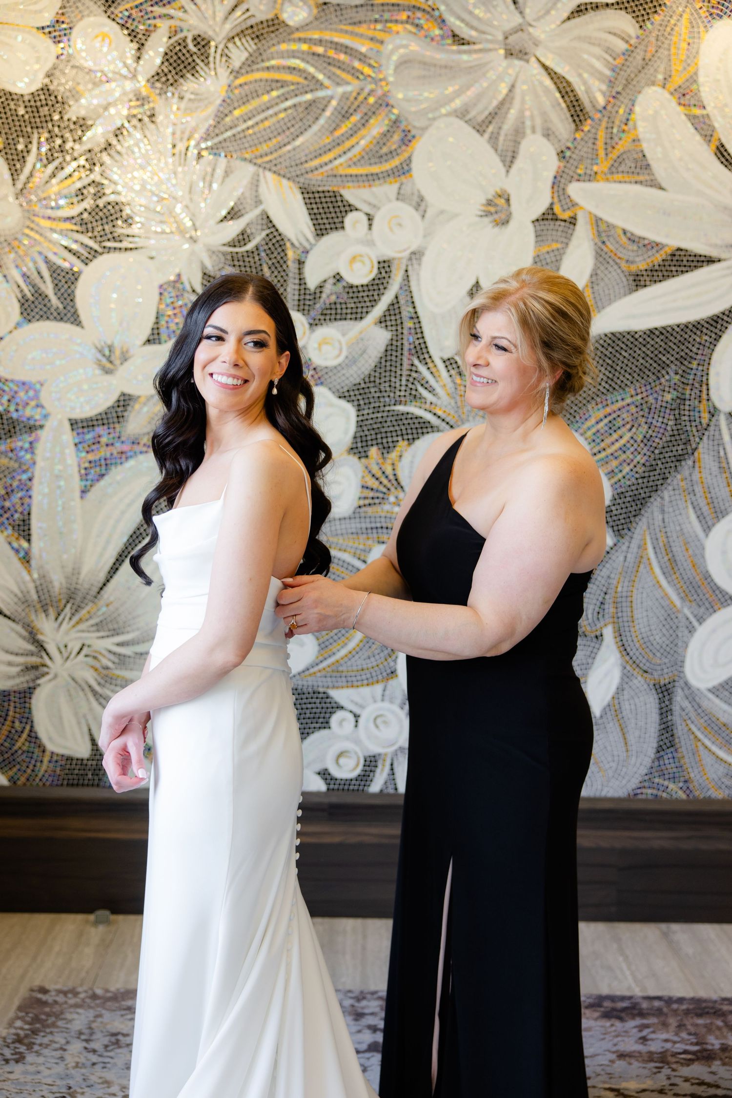 Wedding preparation scene with elegant dresses against a metallic floral wall backdrop.