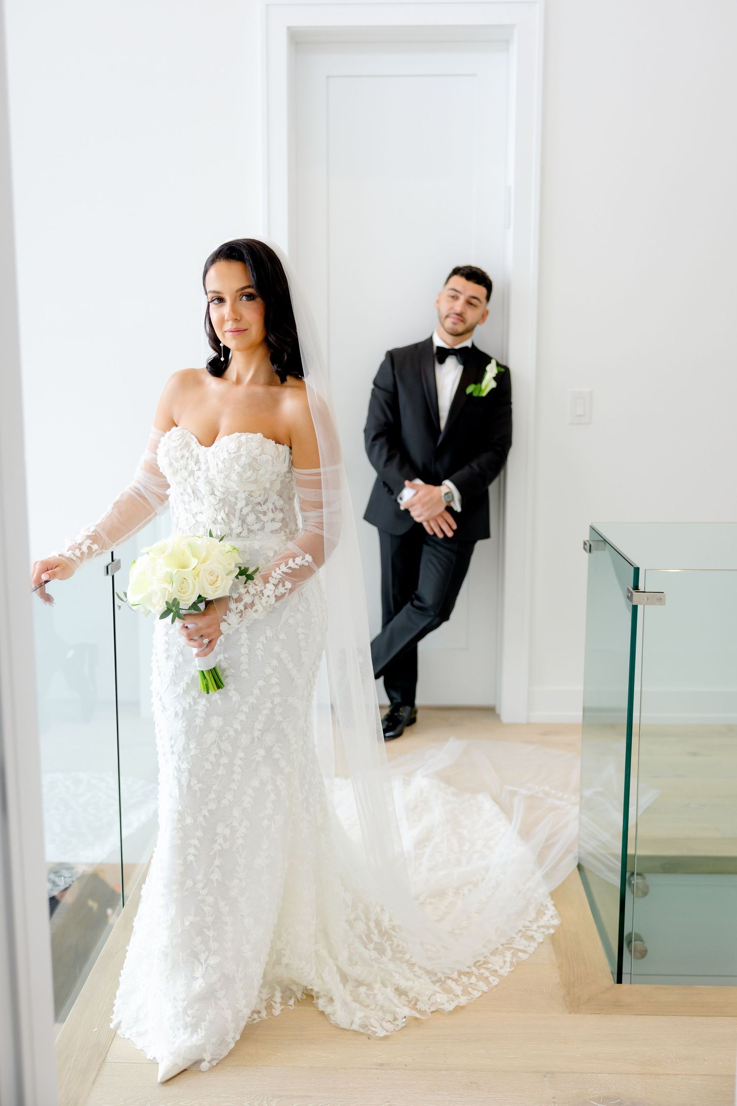 Elegant wedding couple poses on modern staircase with glass railings.