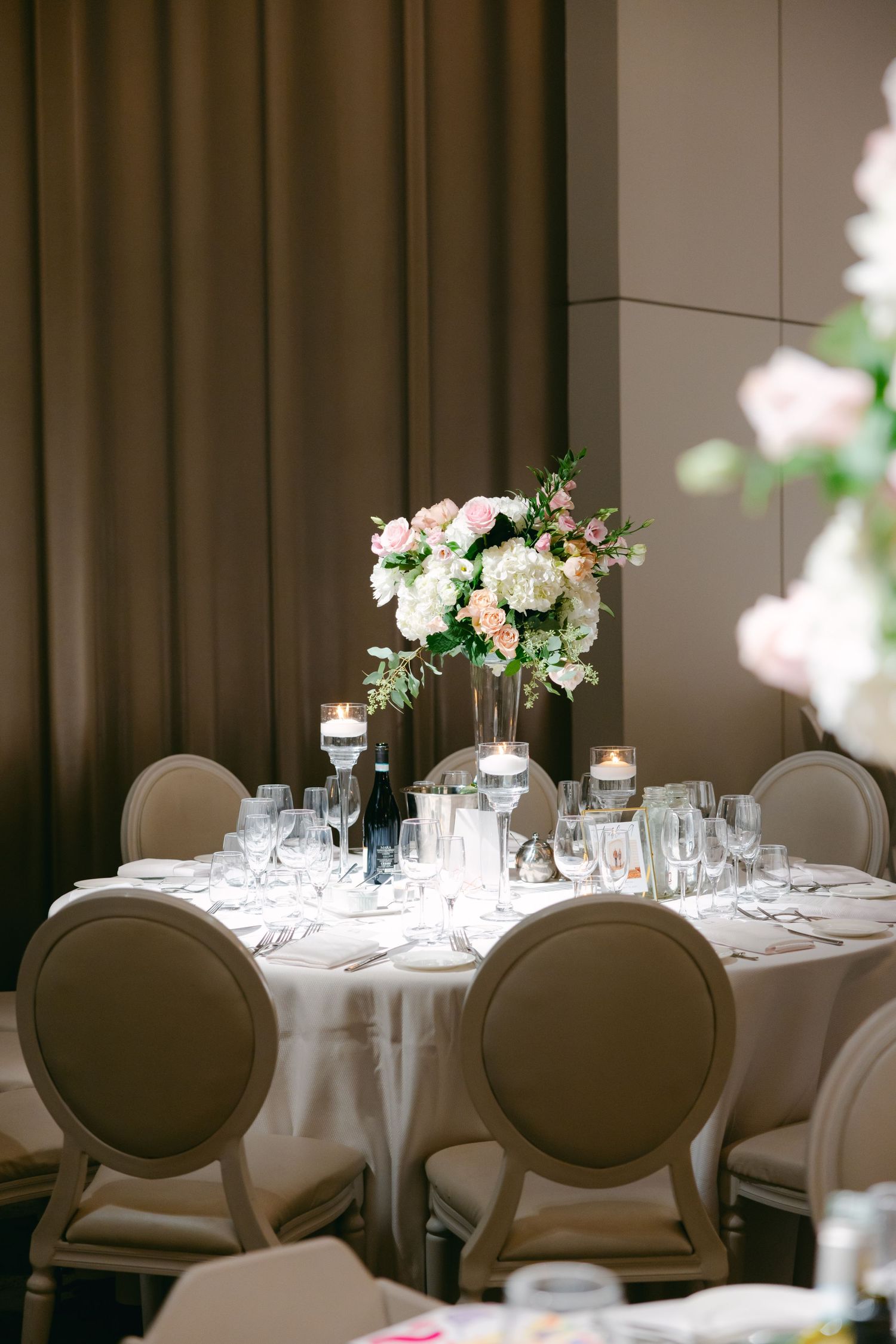 Romantic wedding reception table with white floral centerpiece and elegant place settings.