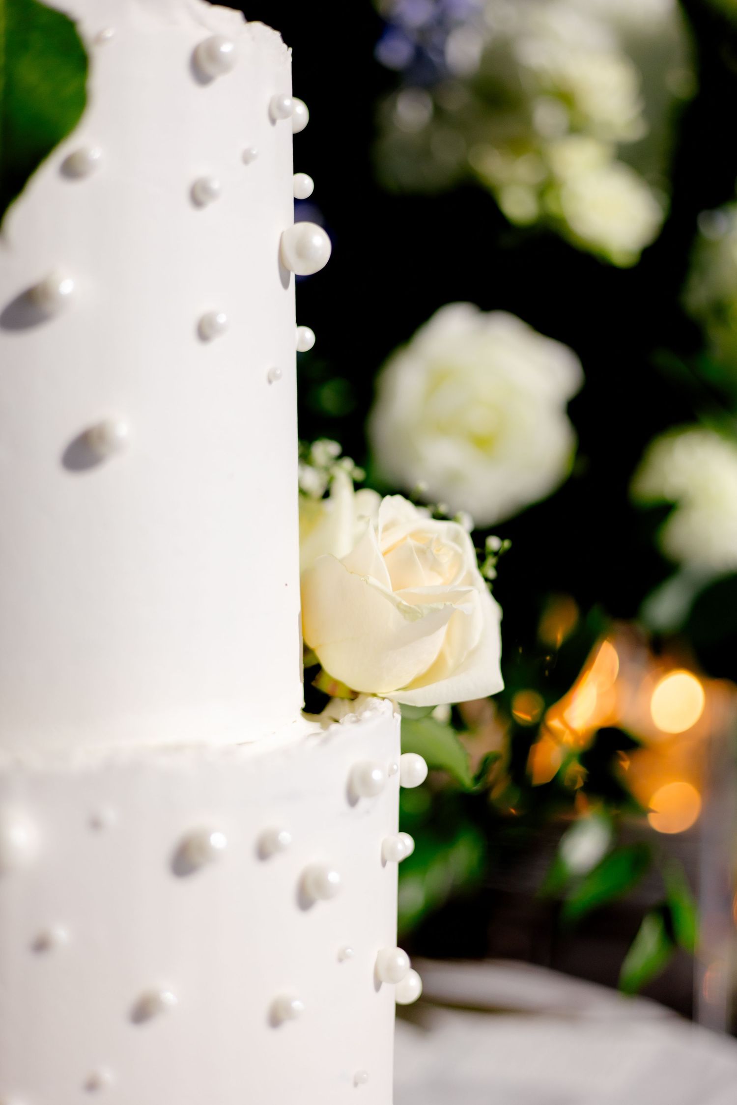 Close-up of white wedding cake with pearl details and delicate rose decorations.