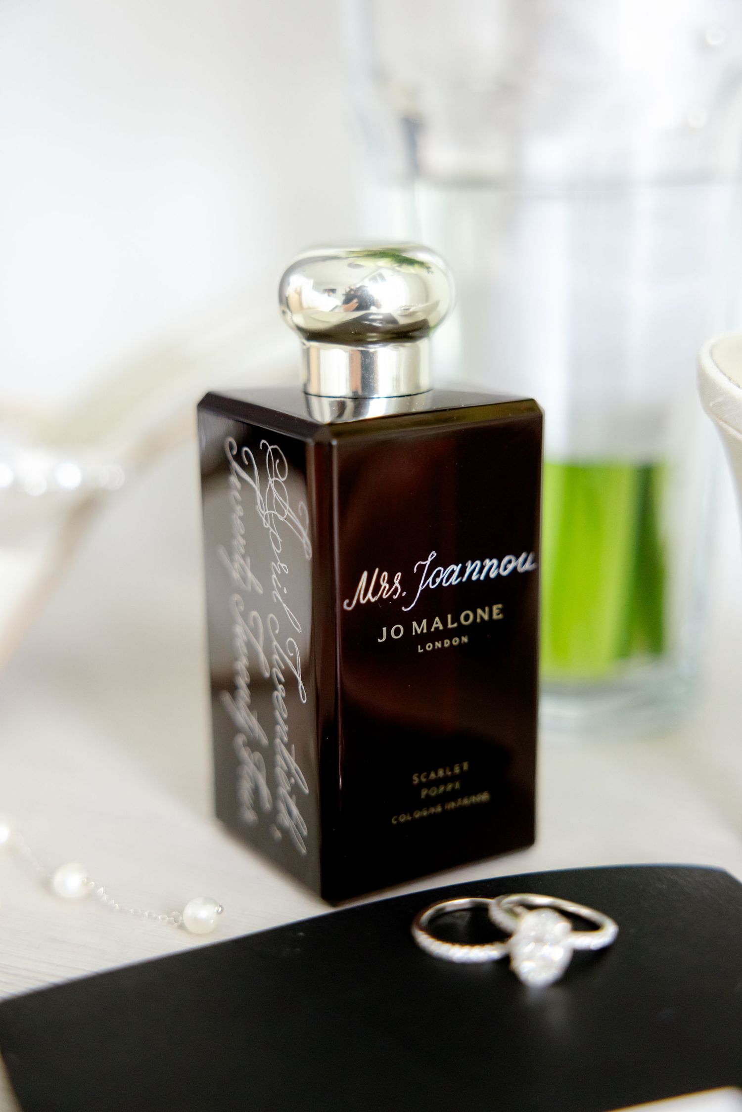Jo Malone perfume bottle and wedding rings displayed on white surface.