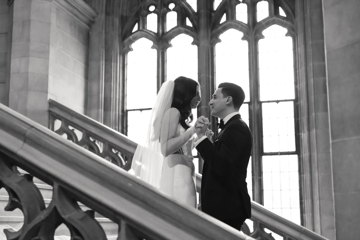A black and white wedding photograph showing an intimate moment against gothic architecture.