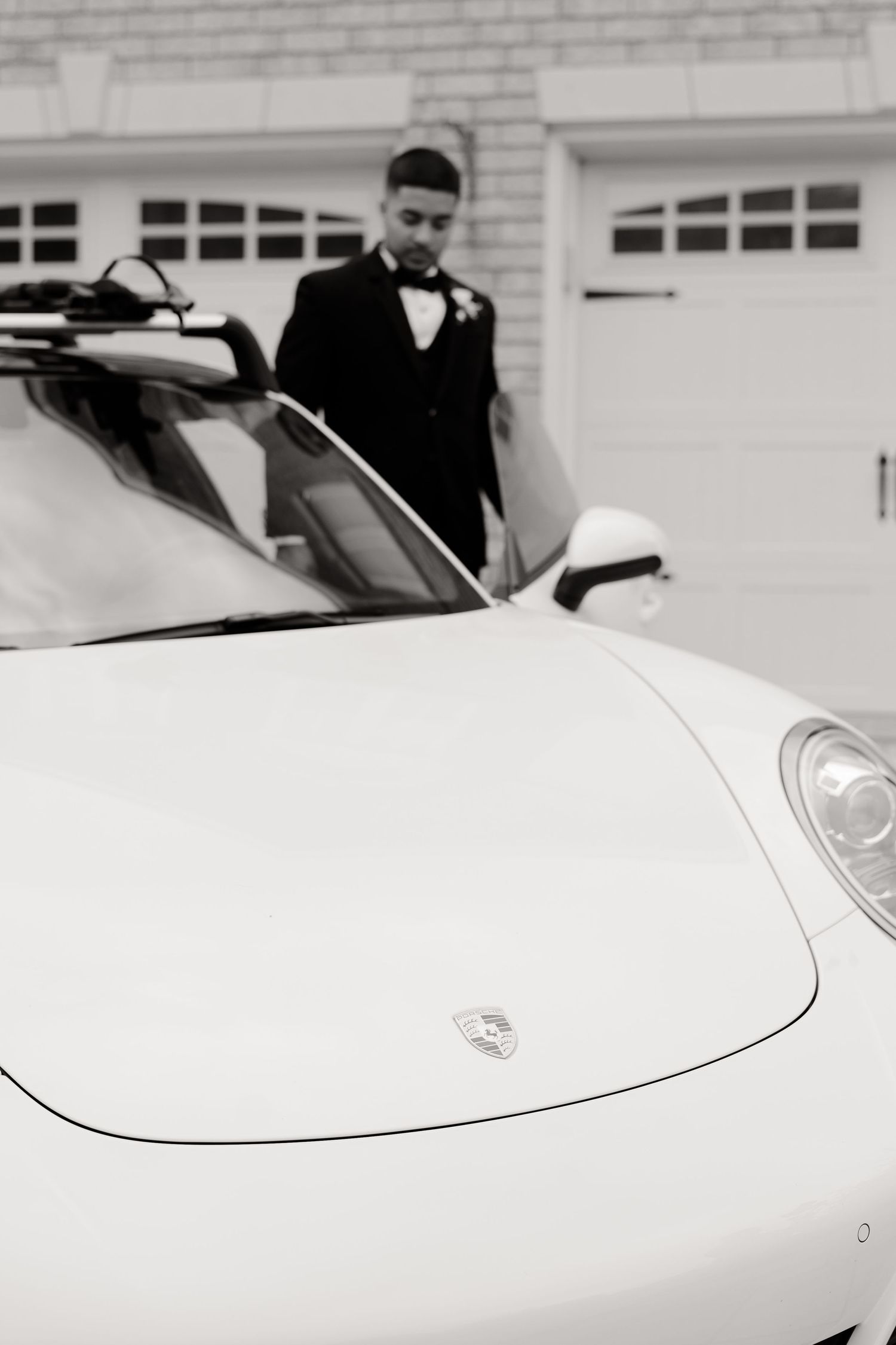 Black and white close-up of a white Porsche with someone in formal attire visible in the background.