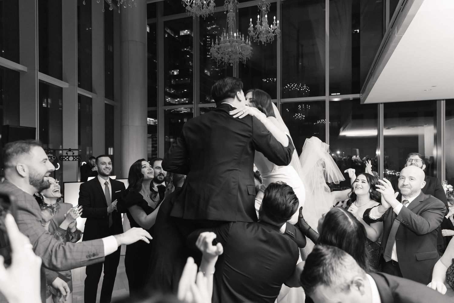 Black and white photo of wedding guests hoisting newlyweds during traditional celebration dance.