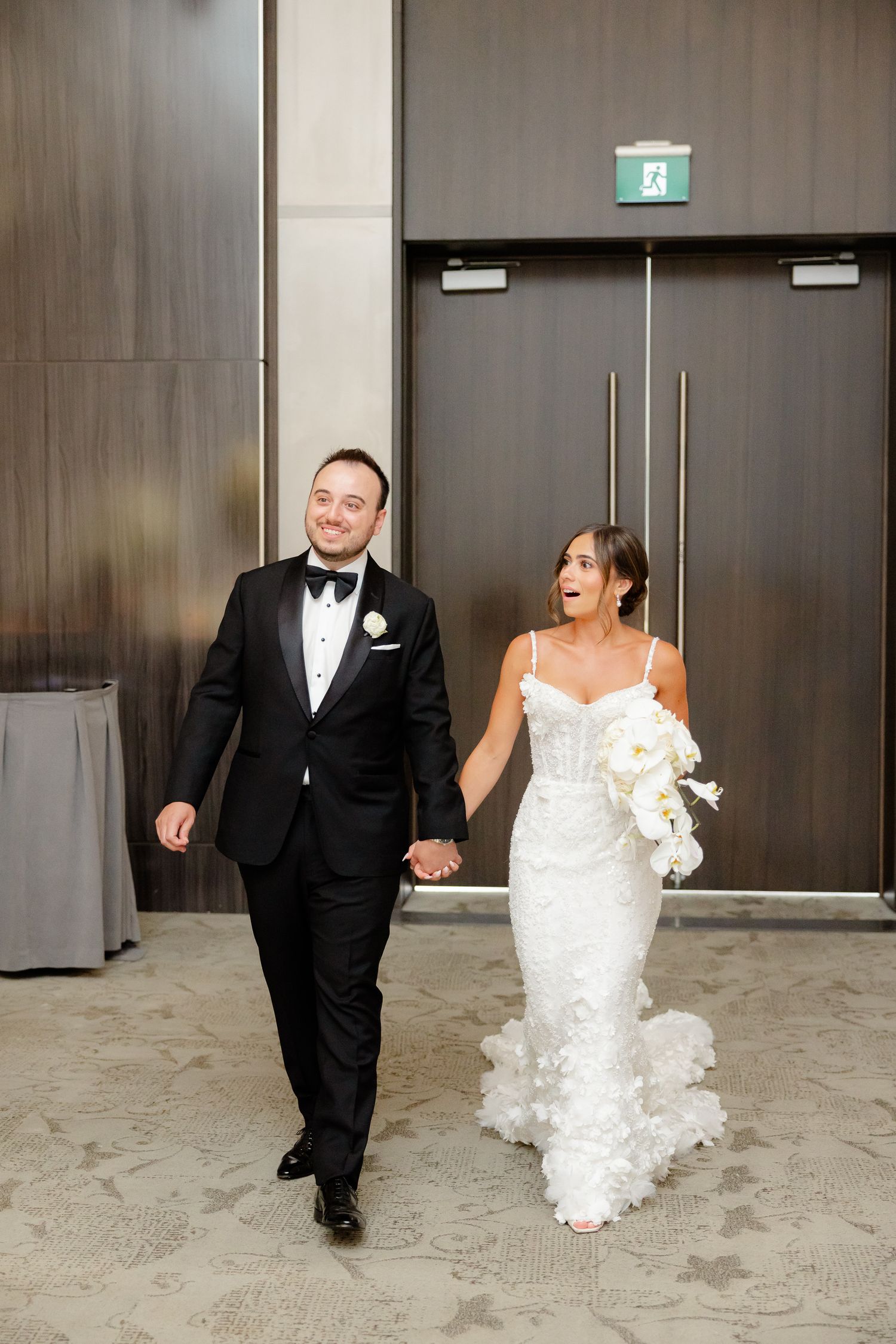 A joyful newlywed couple walking together, the bride wearing a white lace gown and groom in classic black tuxedo.