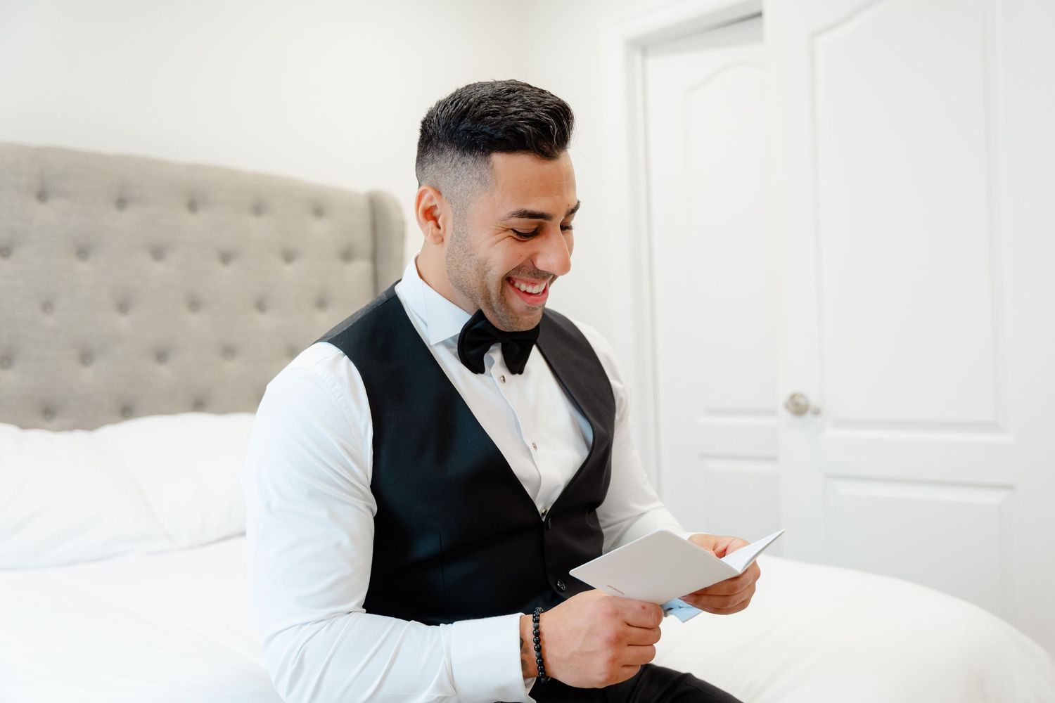 Person in formal attire reading and smiling while sitting on a bed.