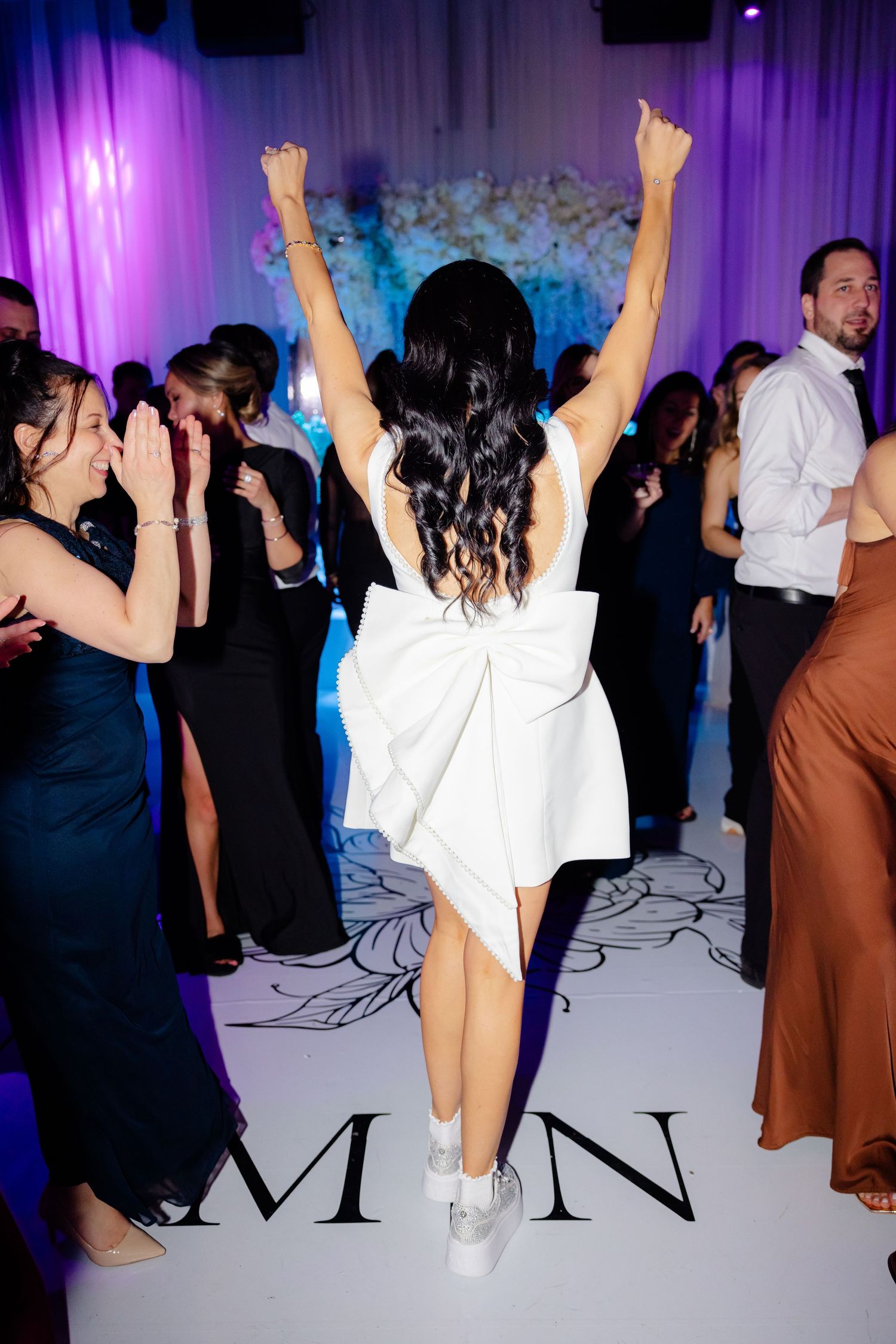 Bride celebrates on dance floor with arms raised during wedding reception.