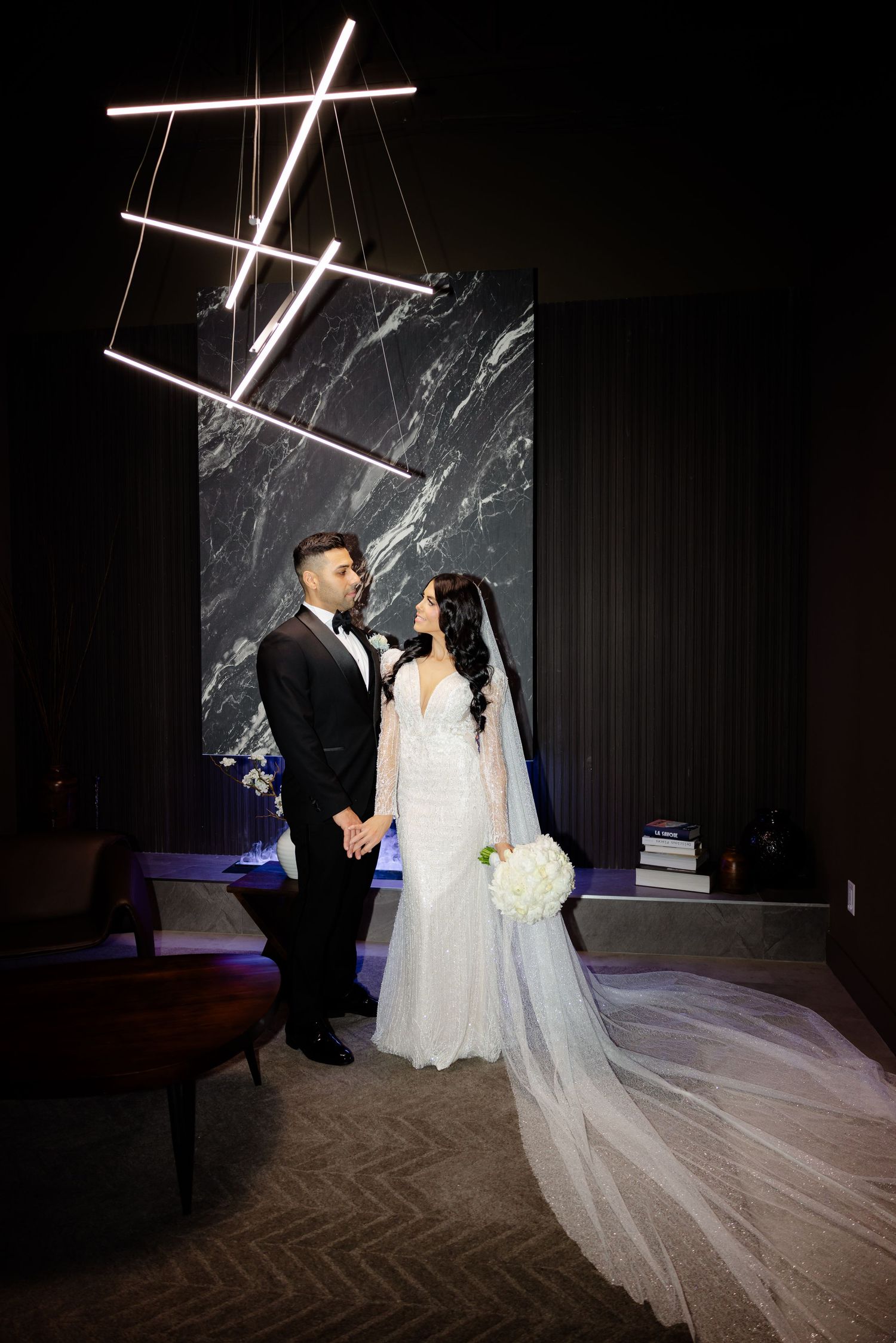 Elegant wedding photo with dramatic lighting and long flowing veil against marble backdrop.