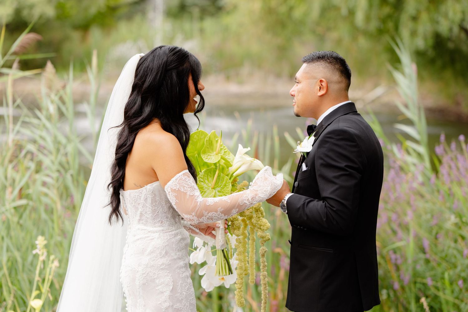 A couple in wedding attire shares a joyful moment together in a lush outdoor garden setting.