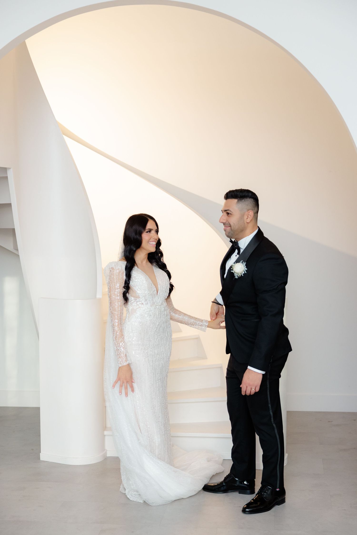 Wedding couple shares intimate moment on elegant white spiral staircase.