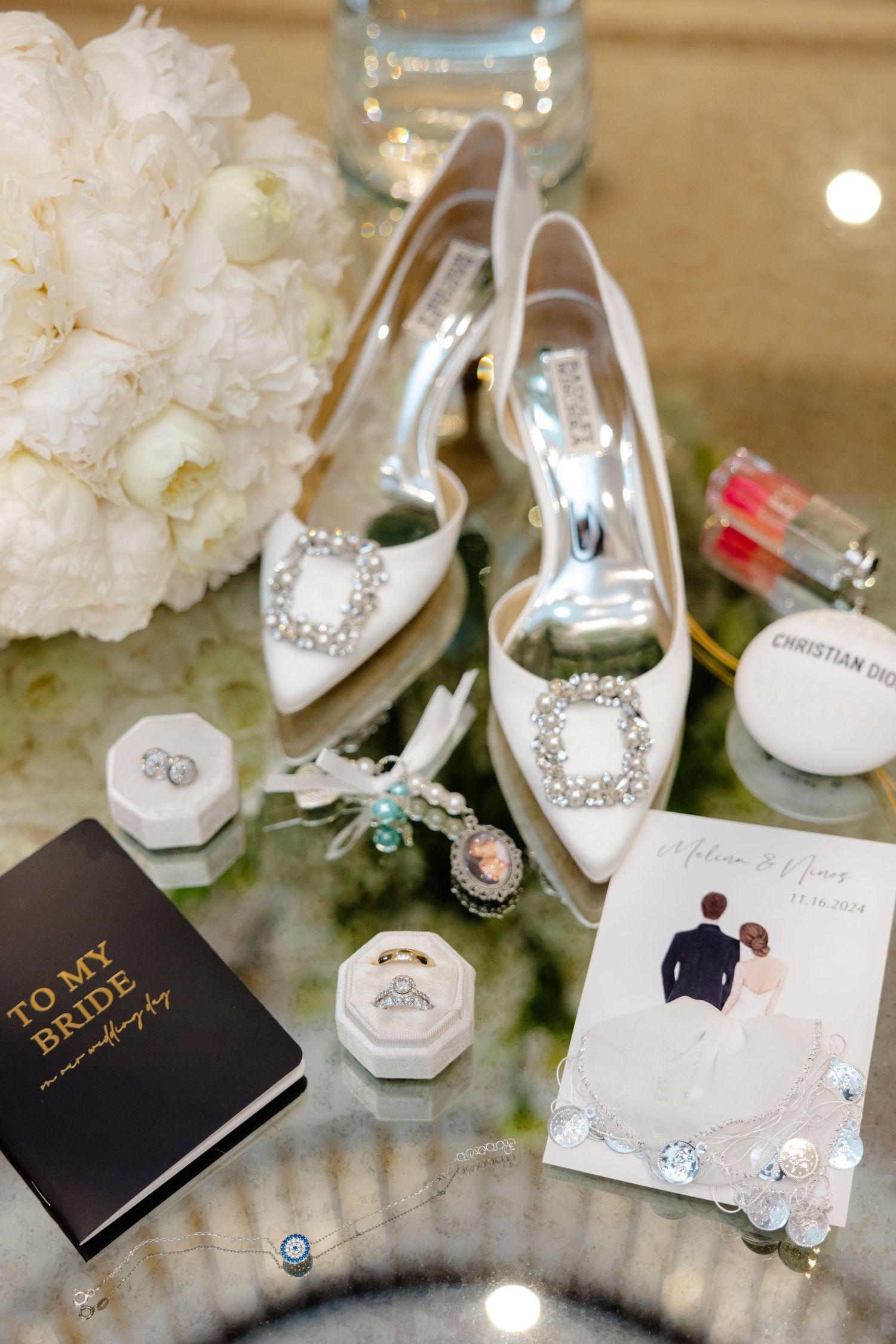 Wedding accessories arrangement with white heels, flowers, and to my bride book on mirrored surface.