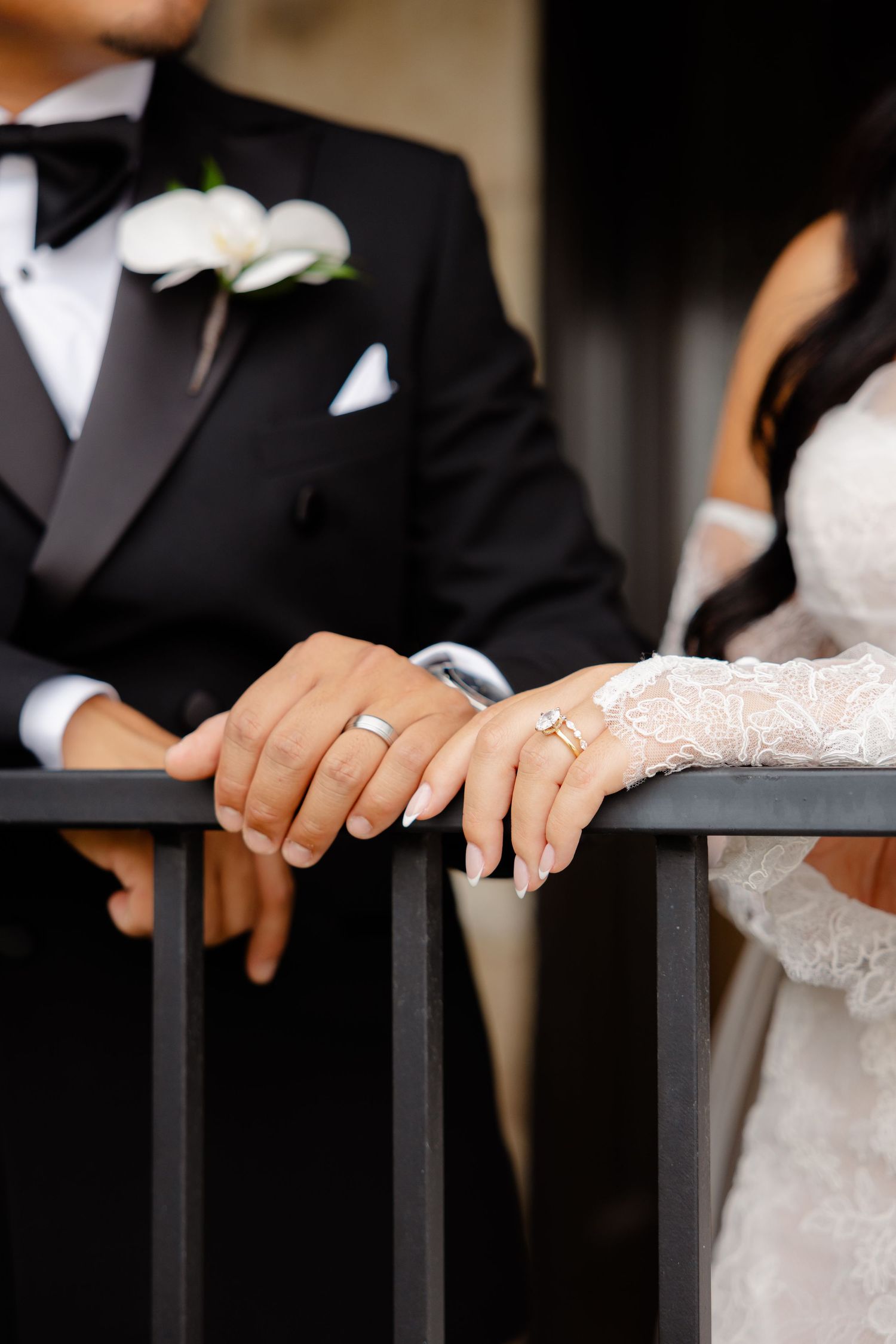Close-up of hands resting on a dark railing, showing white sleeves and black formal attire at a wedding ceremony.