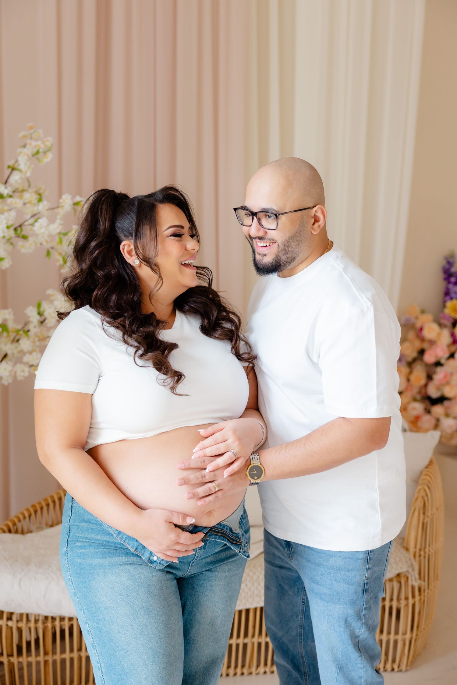A couple wearing matching white shirts and jeans share a joyful moment during their maternity photoshoot.