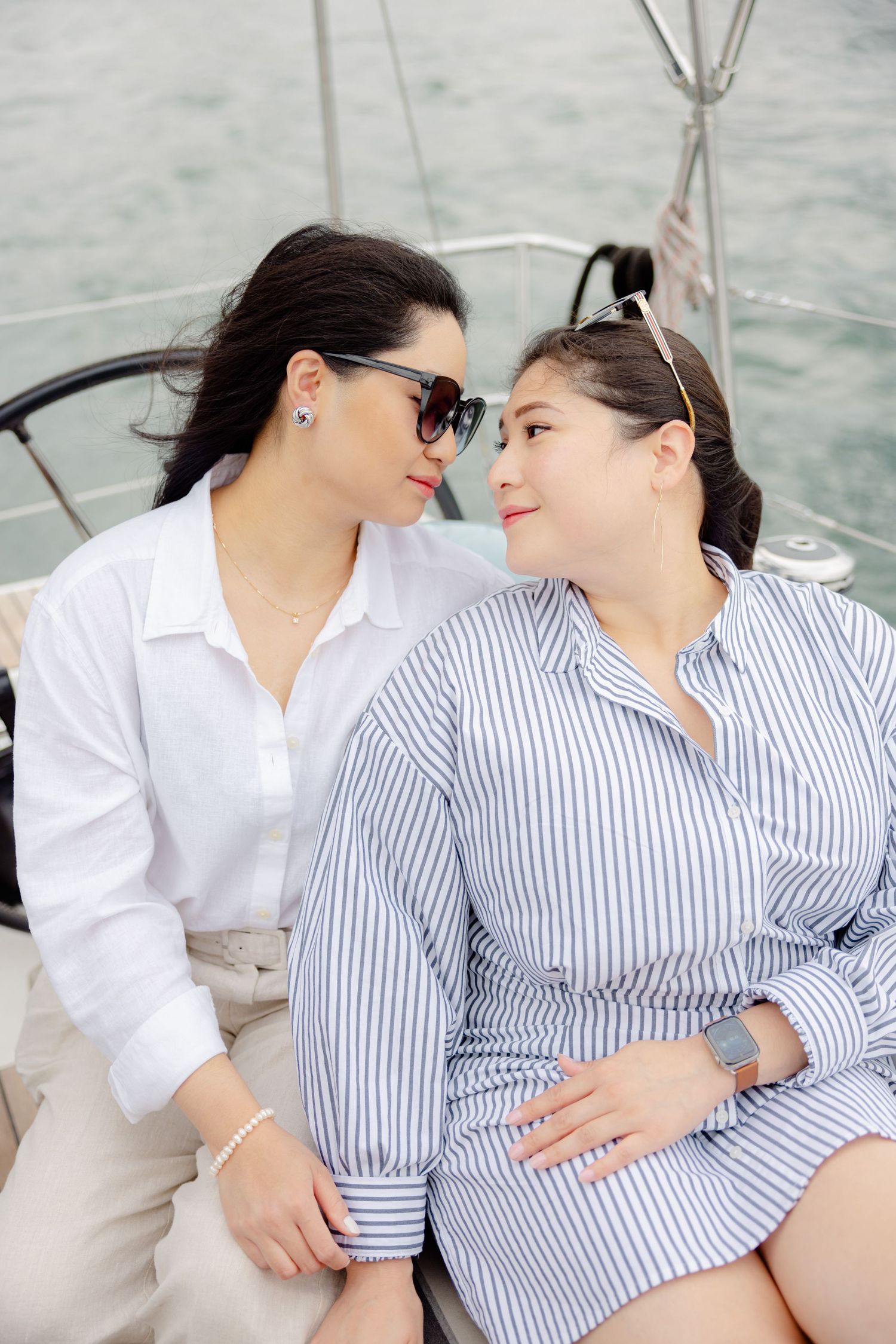 Two people sharing an intimate moment while sitting together on a sailboat, wearing casual button-down shirts.
