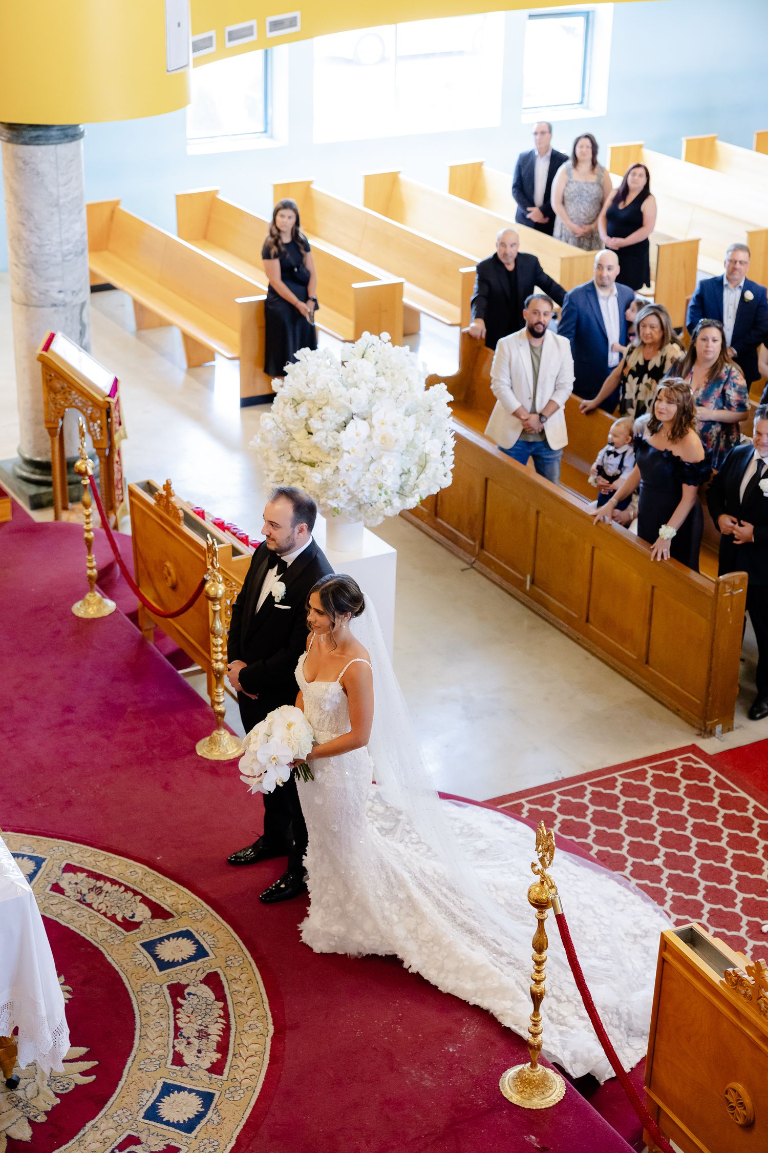 Overhead view of a wedding ceremony in a church with elegant white floral decorations and ornate red carpeting.