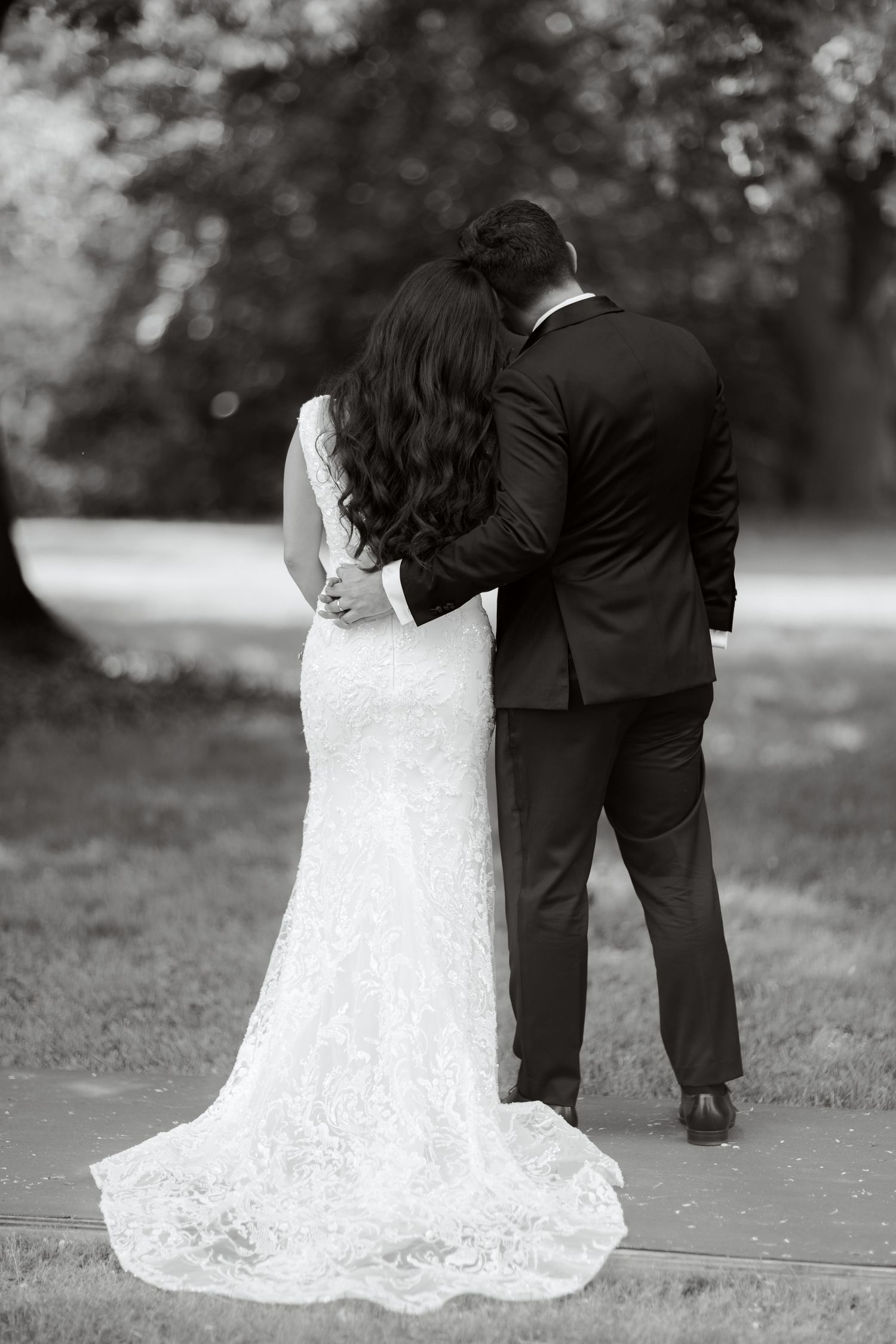 A black and white photo of newlyweds embracing from behind on their wedding day.