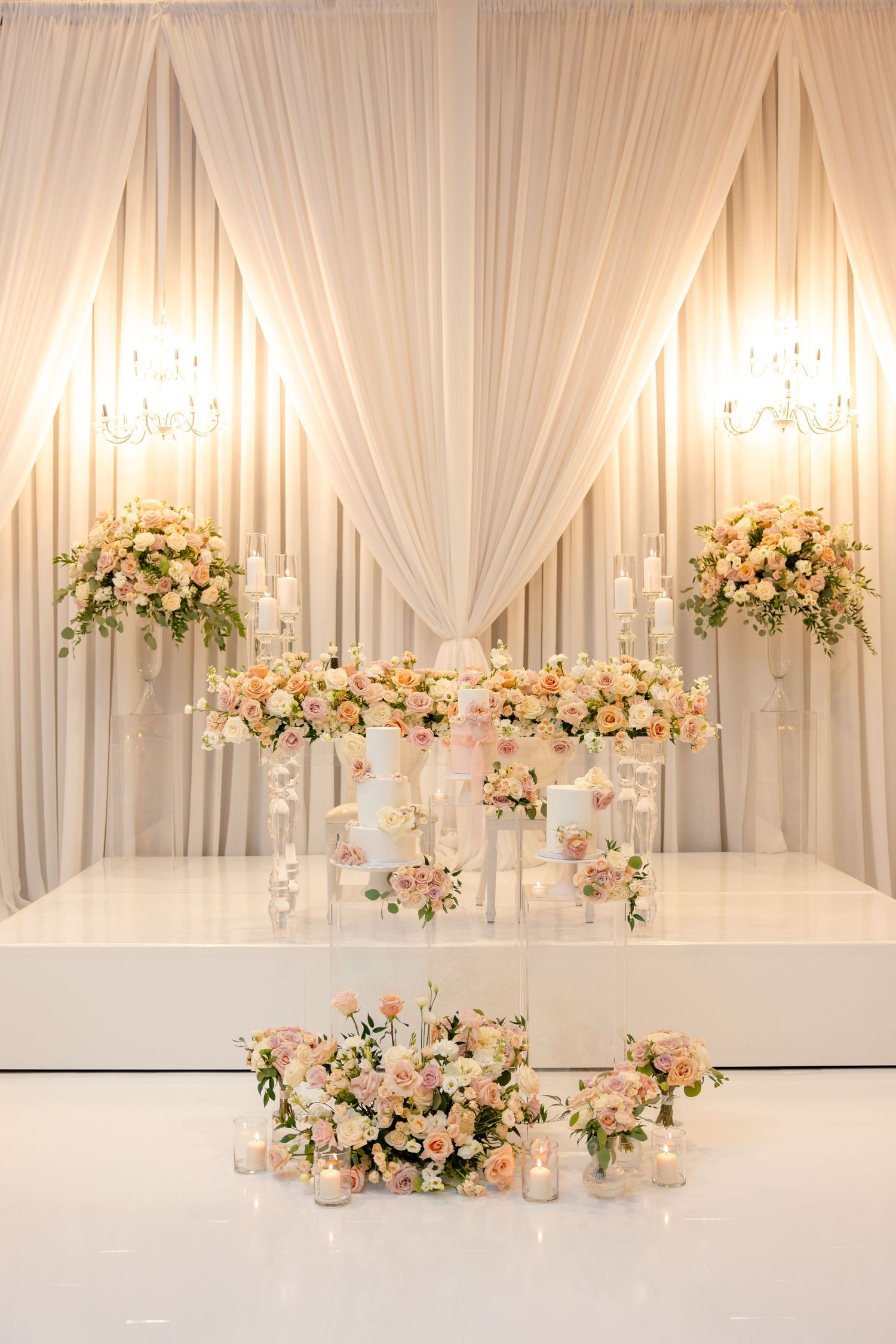 Elegant white draped backdrop with crystal chandeliers and cascading floral arrangements.