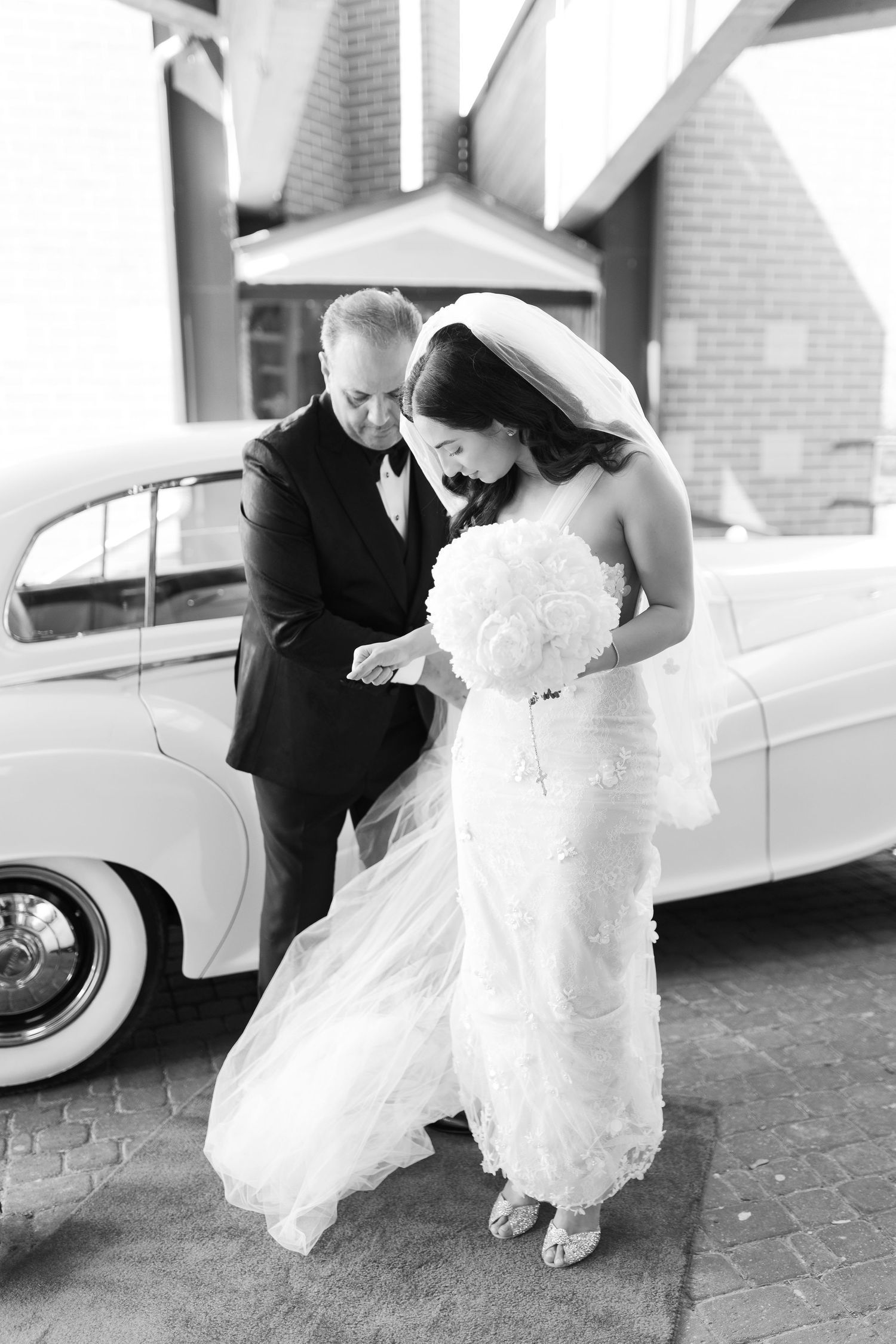 Elegant wedding moment captured in black and white beside classic car.