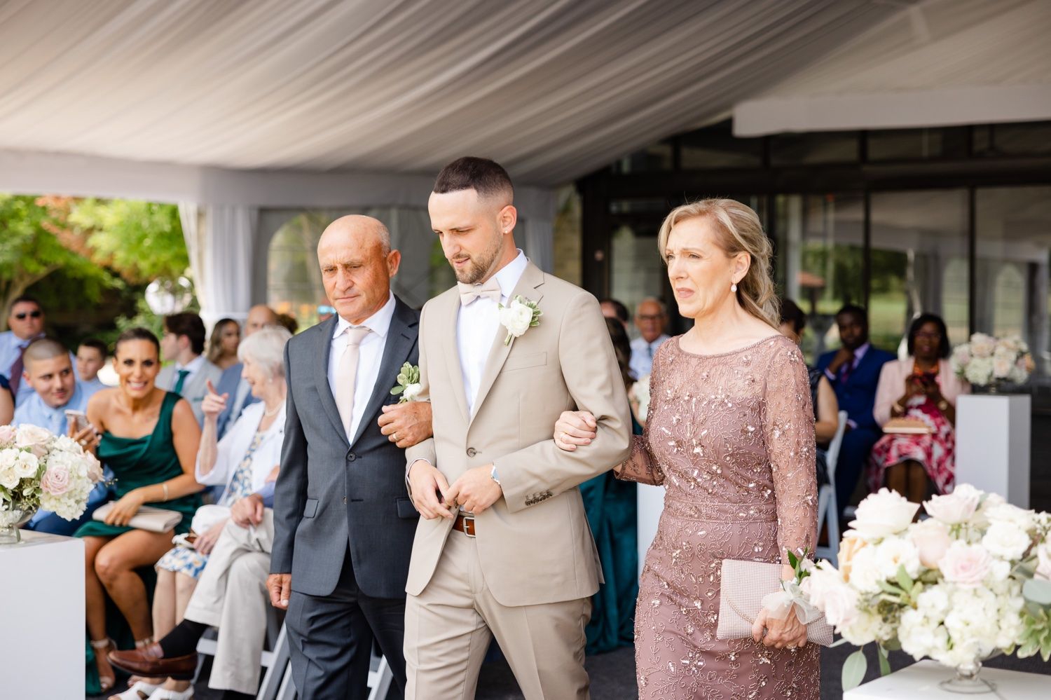 Wedding party members walking down the aisle during an outdoor tented ceremony.