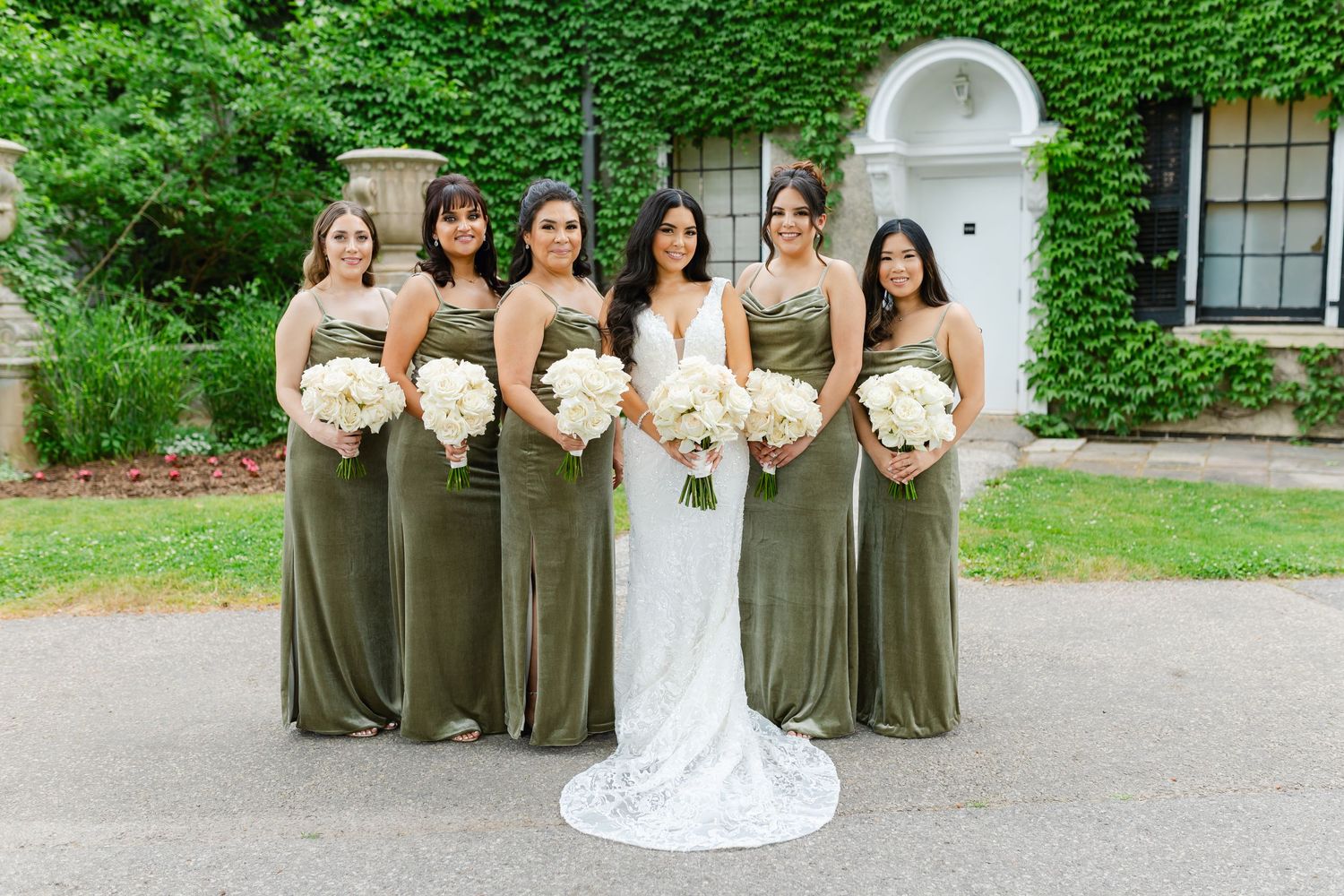 Wedding party in sage green dresses stands with bride in front of elegant white doorway.