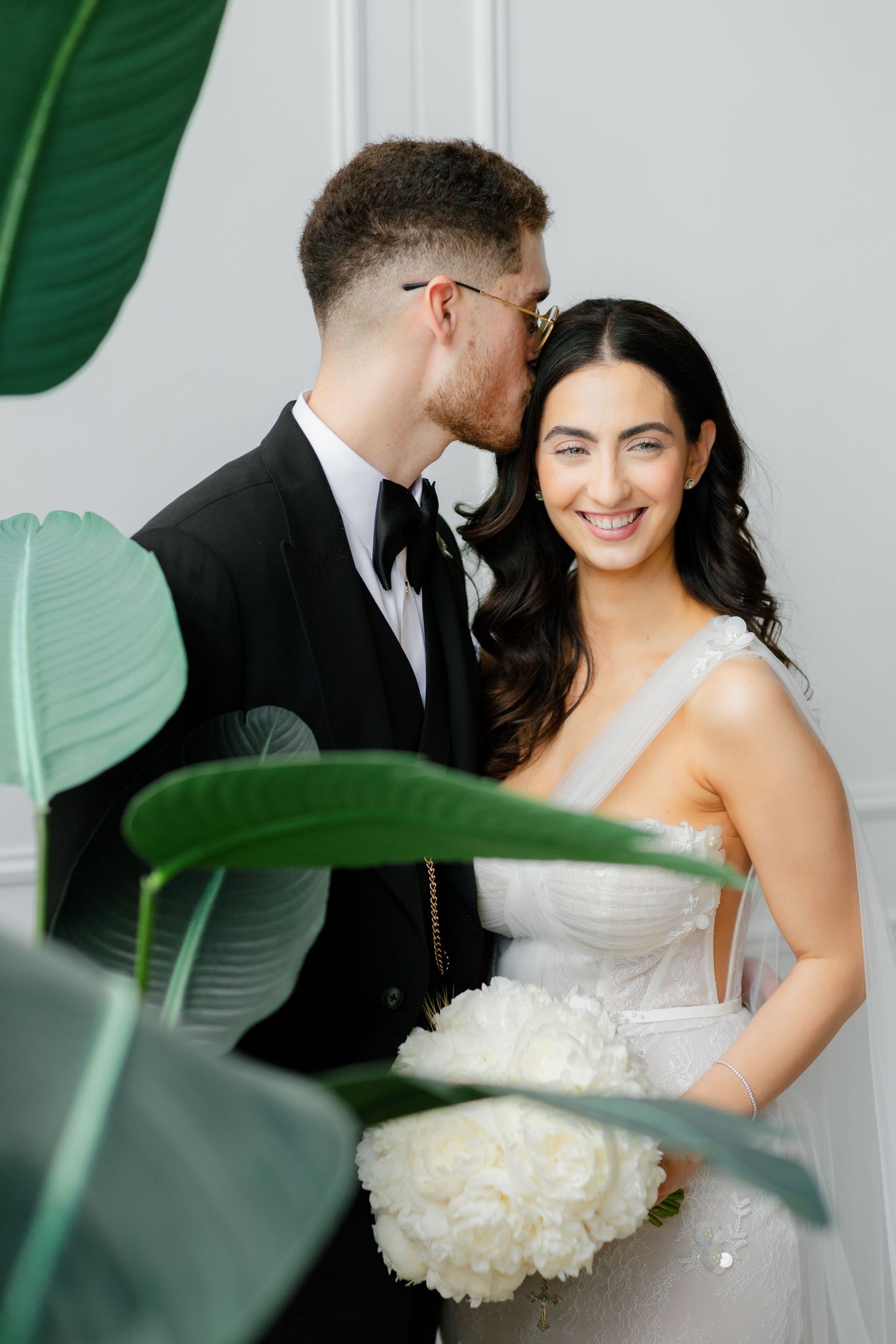 Couple shares intimate wedding portrait moment framed by tropical leaves.