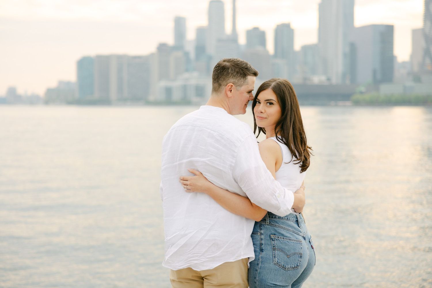 A tender moment between a couple on Toronto's waterfront with the city skyline in soft focus.