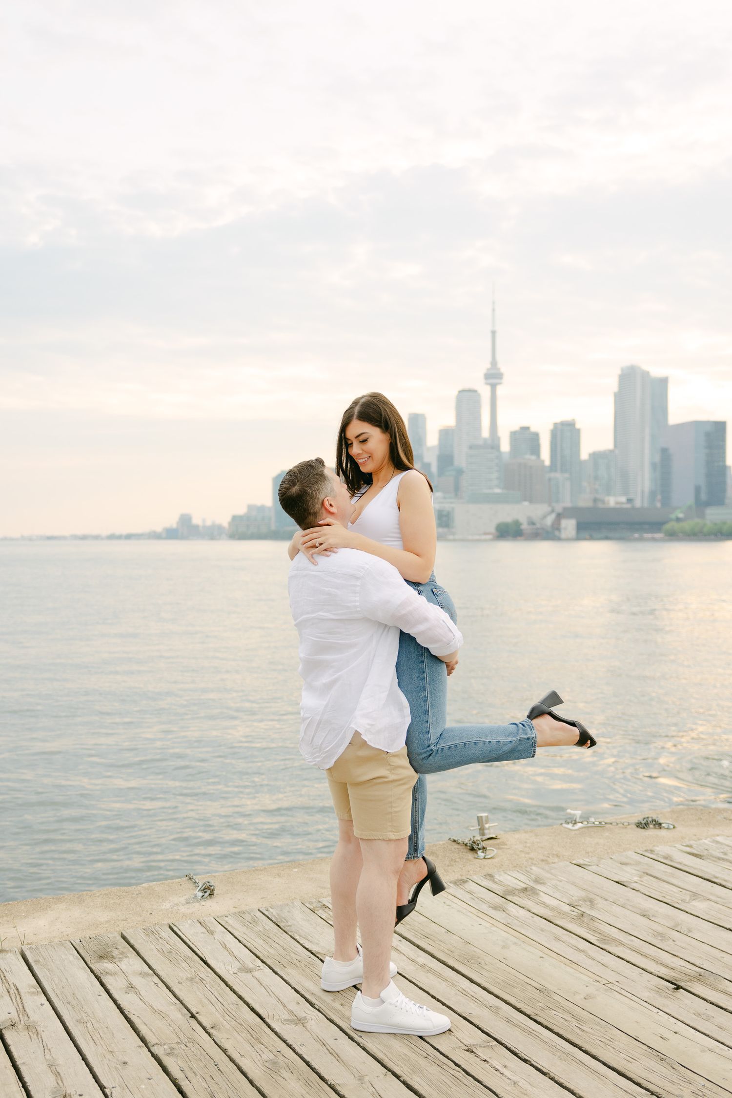 A joyful lift pose on a waterfront boardwalk with Toronto's urban landscape behind.
