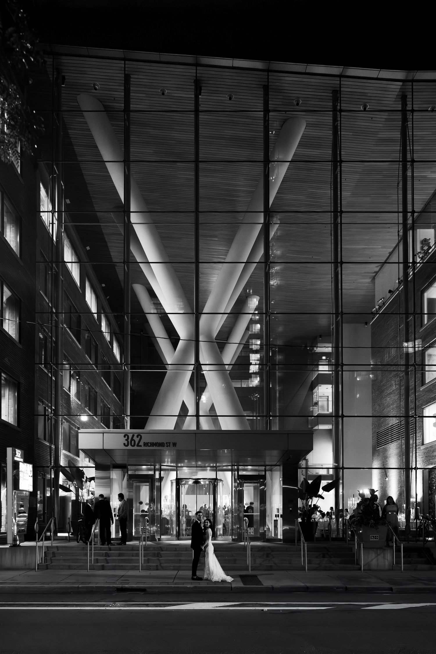 Black and white architectural photo of modern building entrance with dramatic lighting and X-shaped support beams.