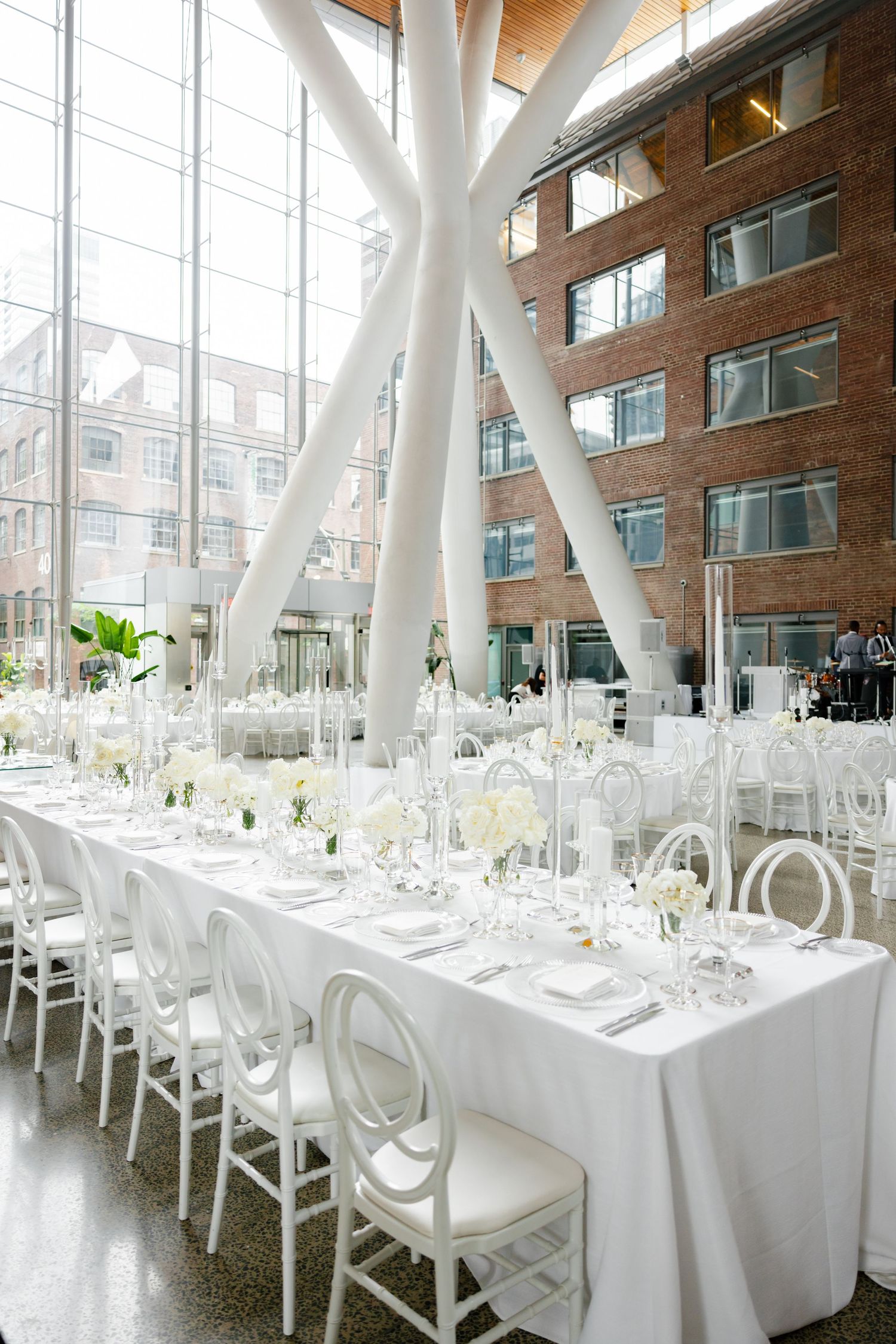 Elegant wedding reception setup with long white tables and modern architectural columns in an industrial-chic venue.