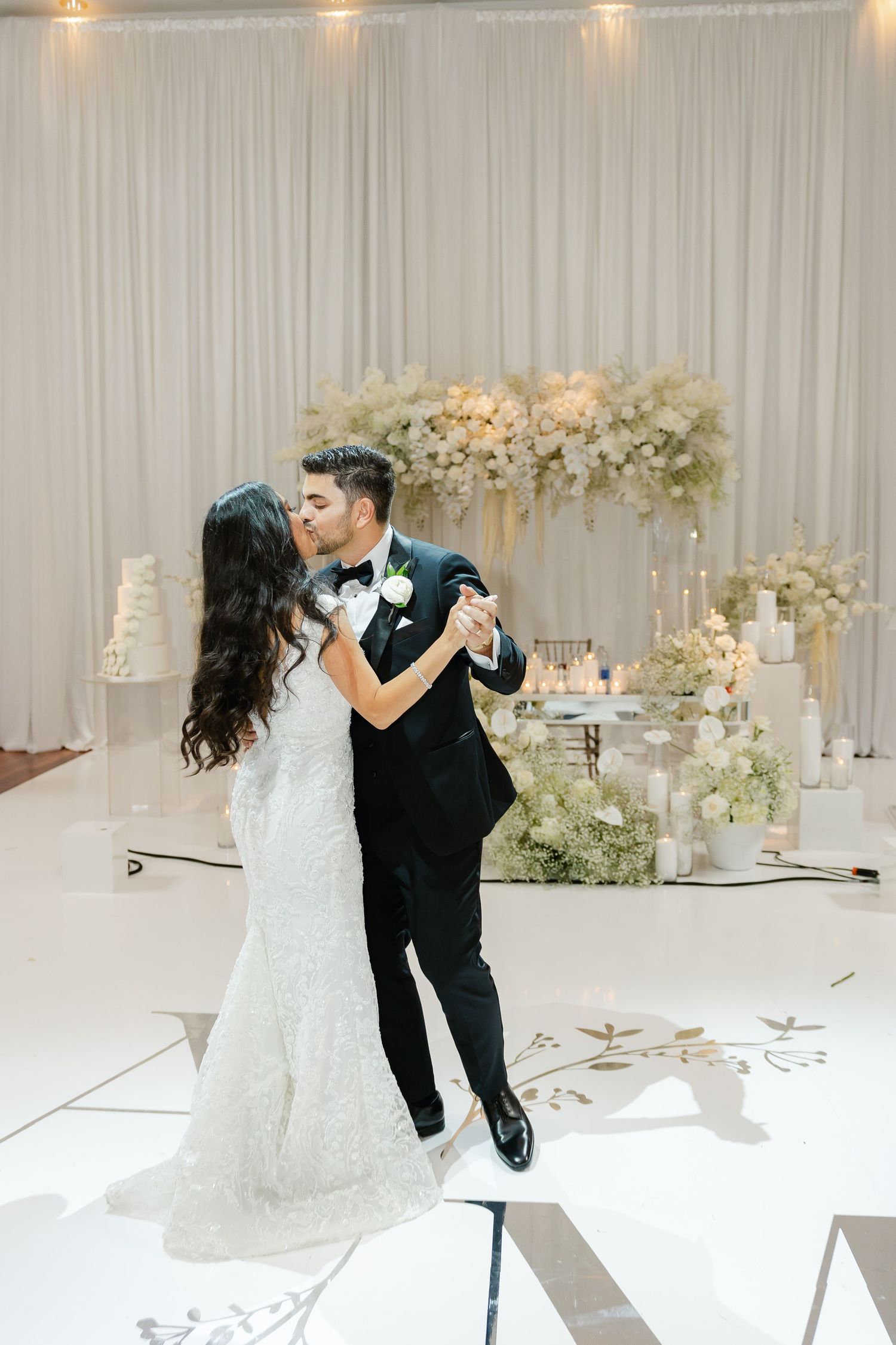 Newlyweds share an intimate dance on their wedding day surrounded by elegant white floral arrangements.