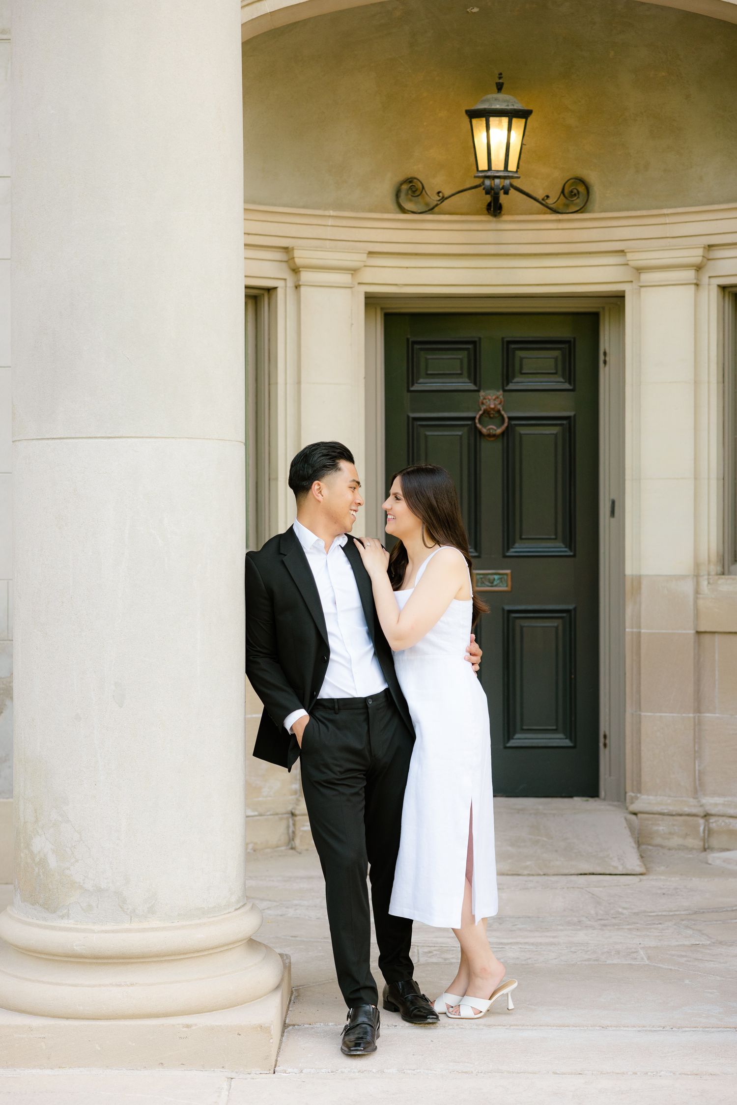 Romantic couple in black and white formal wear share intimate moment by classic architectural entrance.