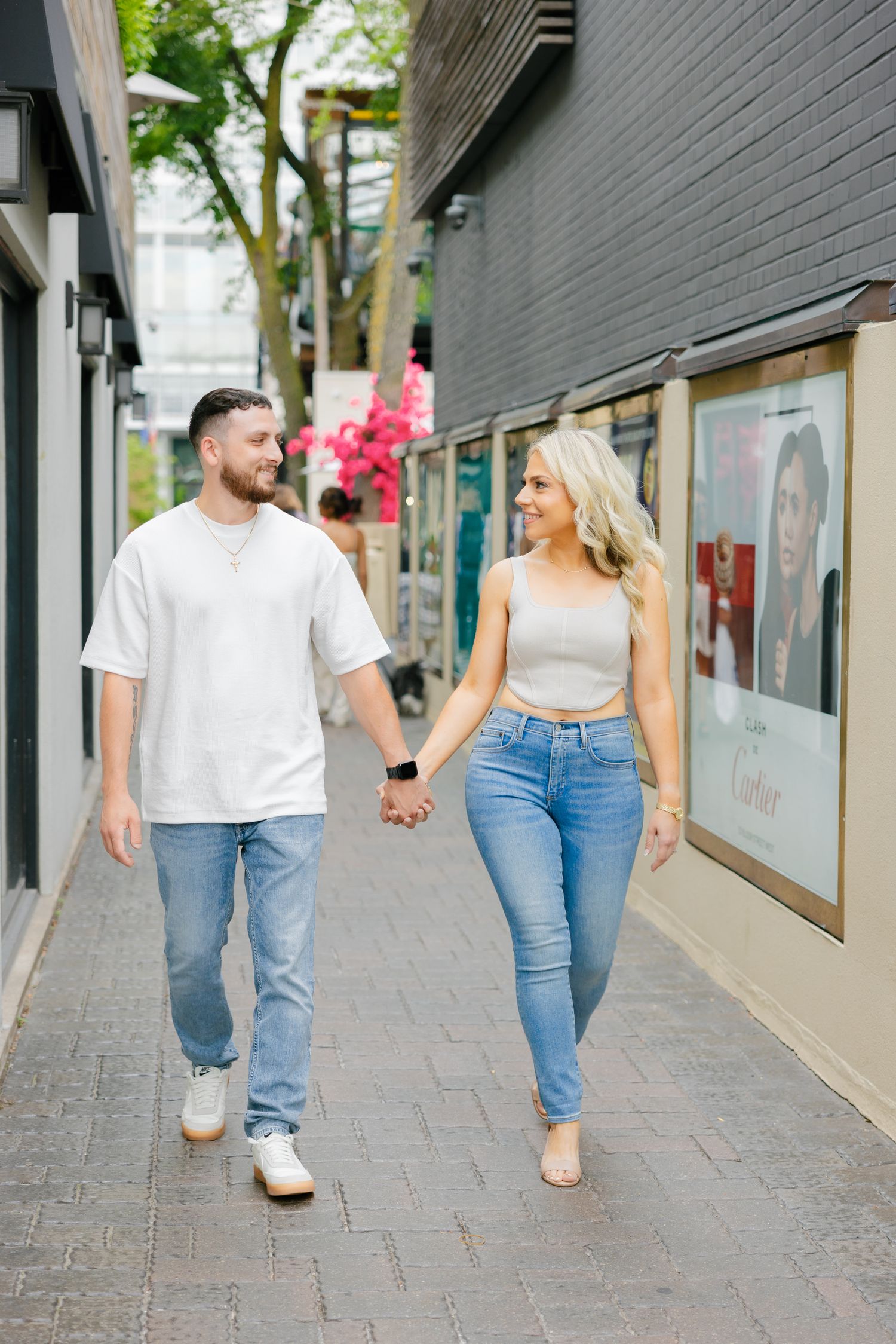 A couple in coordinated outfits walking together on a brick pathway past retail displays.
