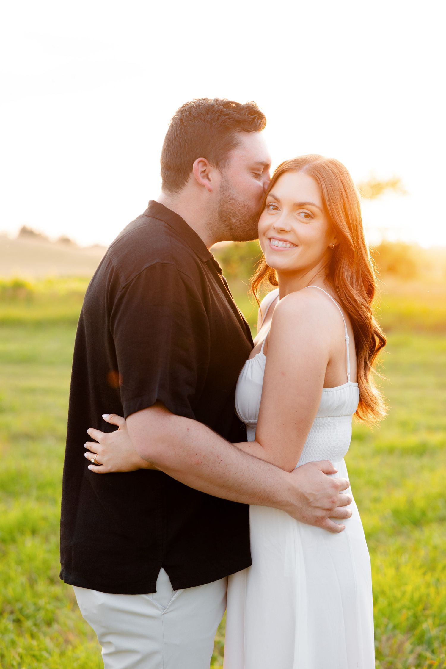 Loving couple shares joyful moment during sunset engagement session in meadow.