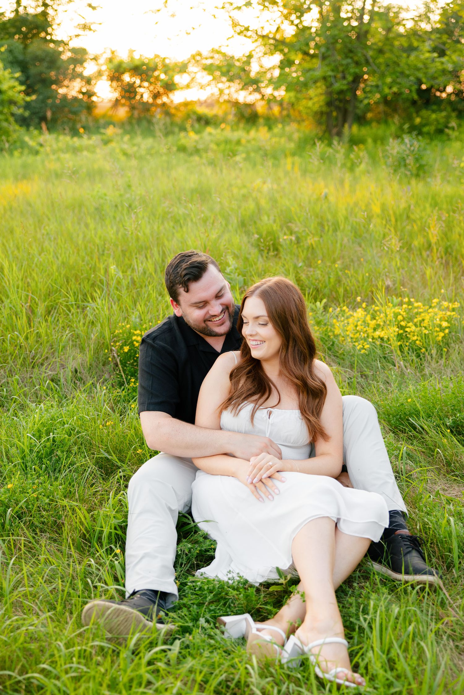 Happy couple laughs together during golden hour photoshoot in a meadow.