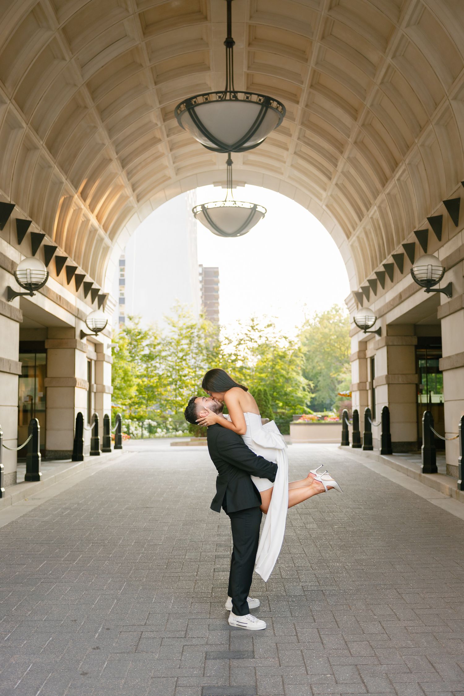 Couple in formal attire sharing a romantic moment under an architectural archway with natural lighting.