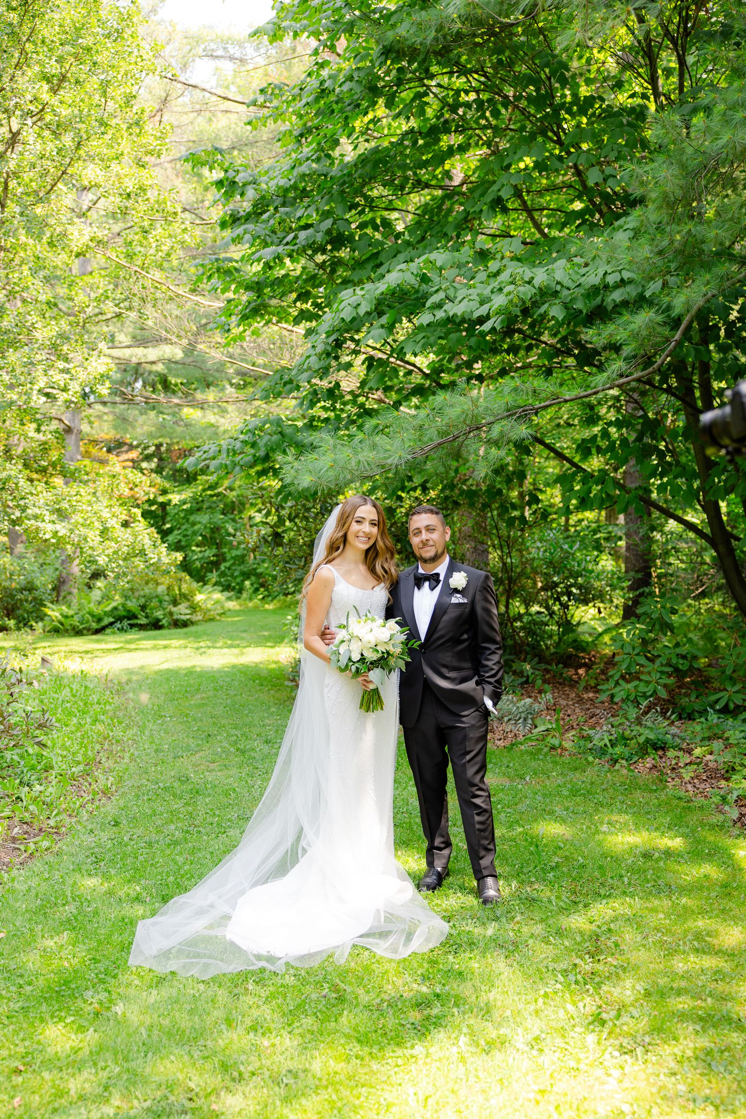 Elegant garden wedding portrait with couple standing on grass path surrounded by trees.