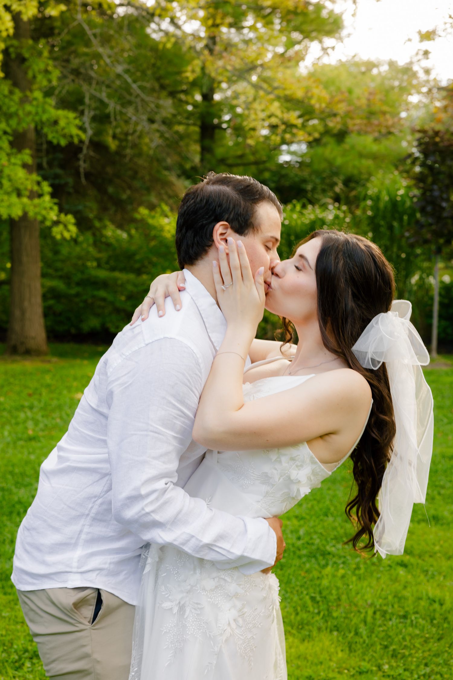 A romantic wedding couple sharing a tender kiss in a lush green garden setting.