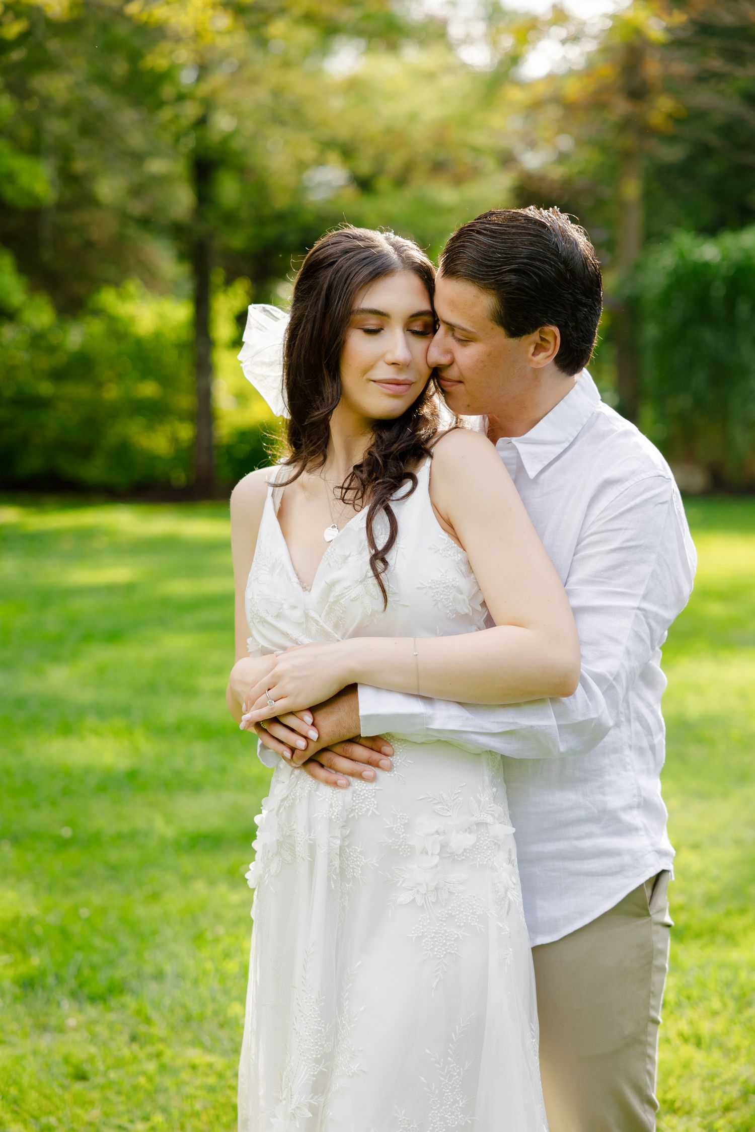 An intimate moment shared between a couple in a white dress and shirt against garden greenery.