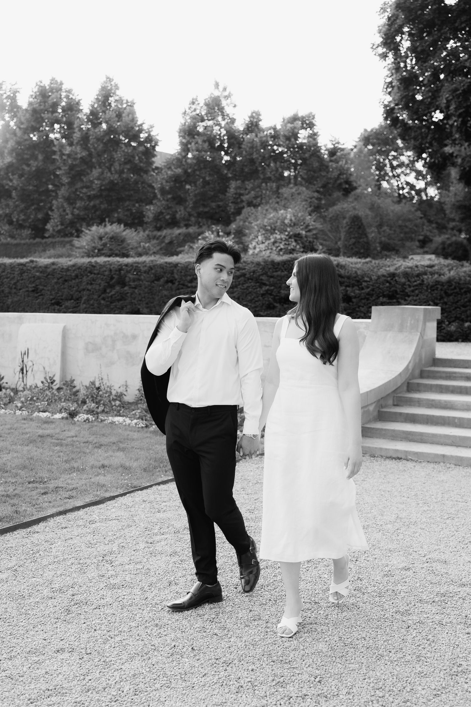 A black and white capture of a couple holding hands while walking in a formal garden setting.