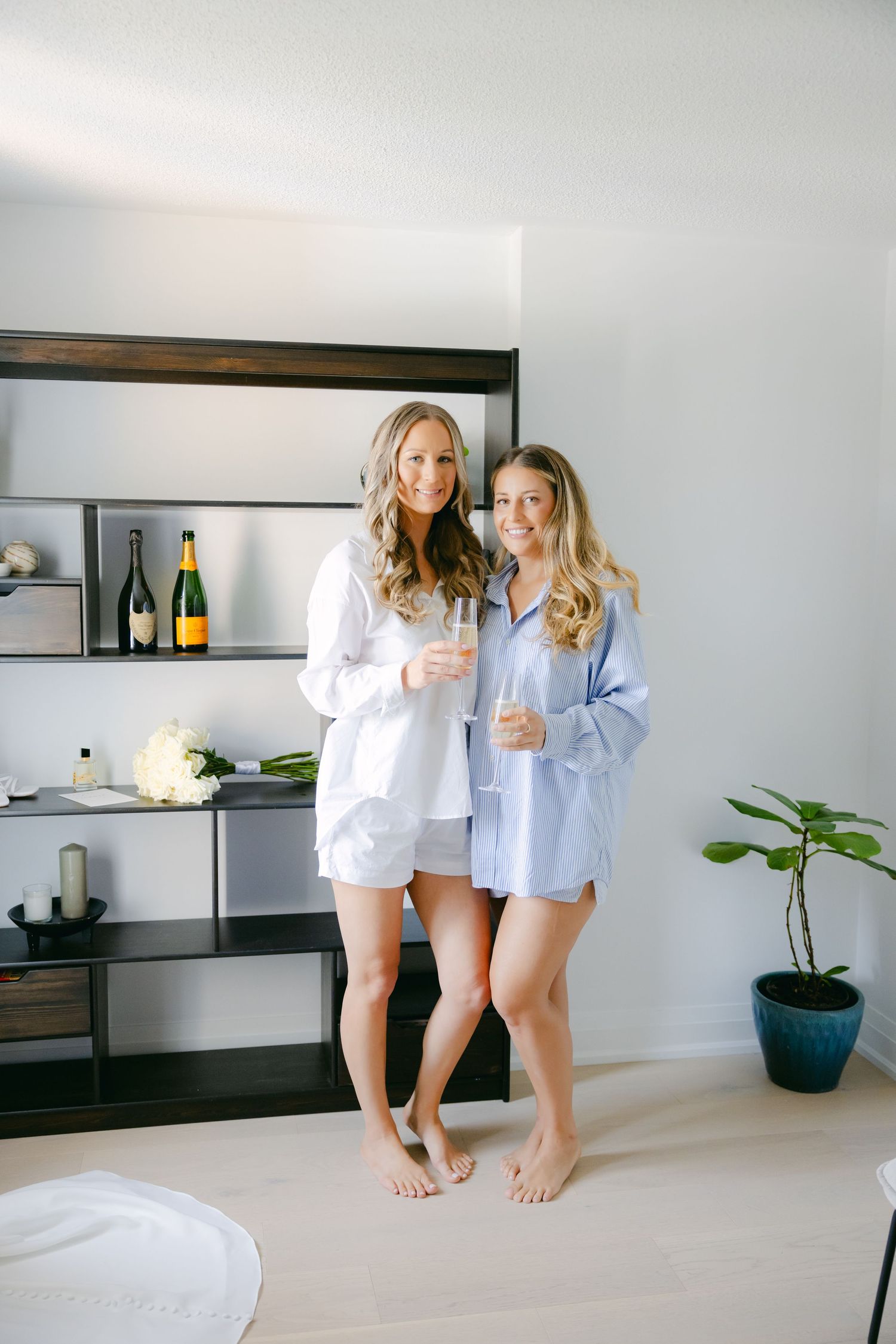 Two people in casual sleepwear standing barefoot in a modern room with shelves.