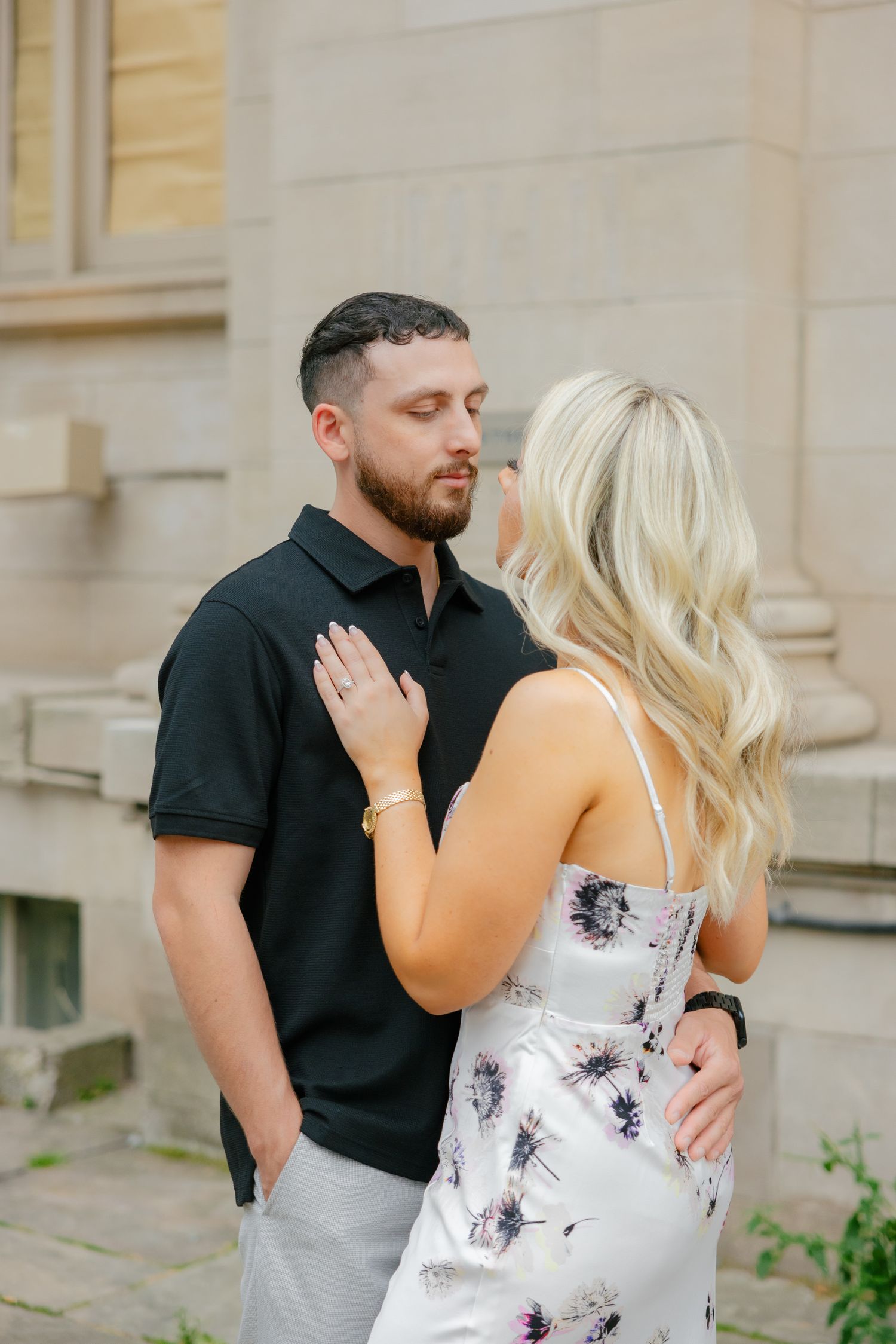 Romantic couple embracing outside historic building with woman in floral dress.
