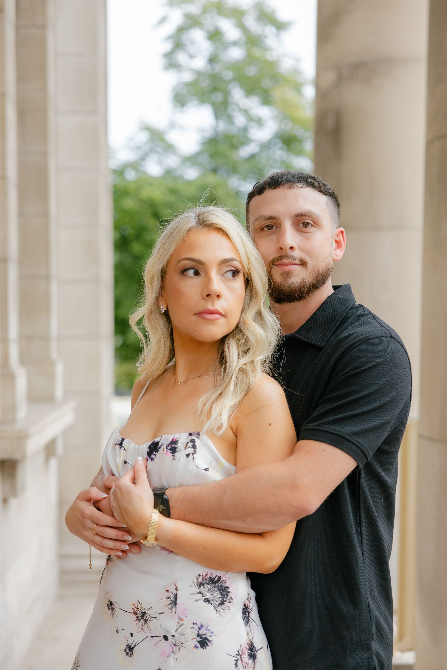 Elegant couple embraces while posing between classic architectural columns in summer.