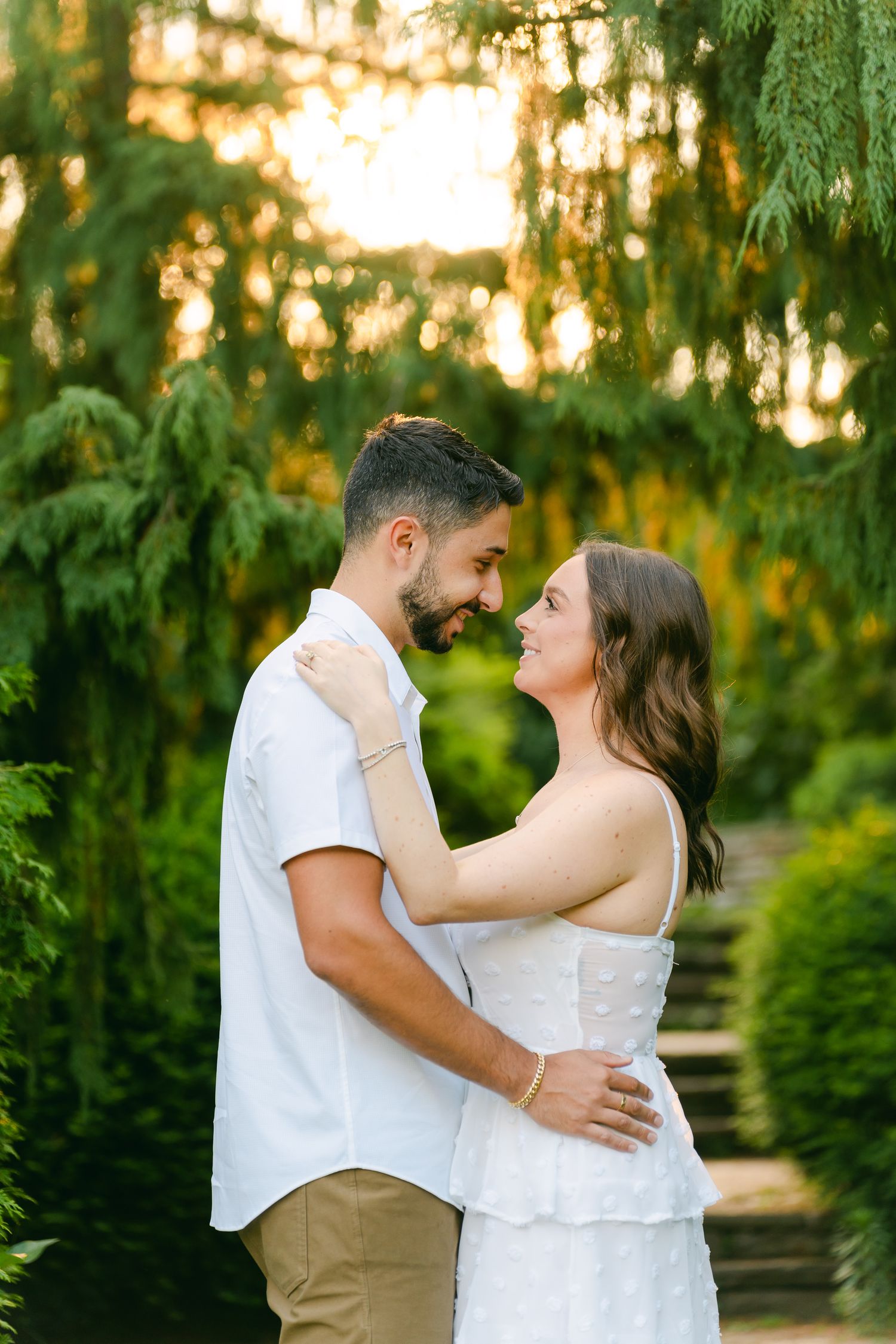Tender embrace shared between a couple on a stone pathway with golden sunset filtering through trees.