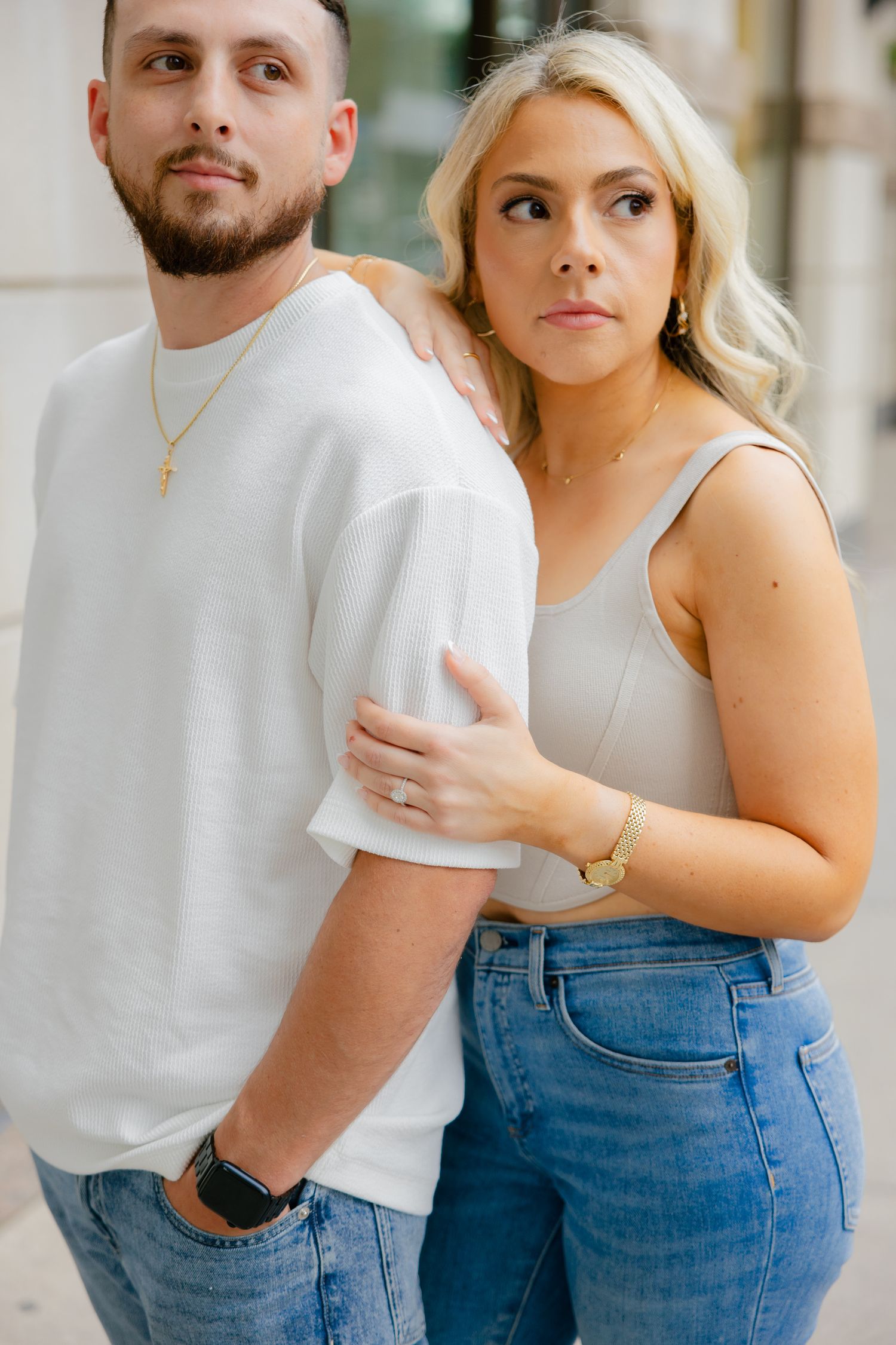 A couple in casual attire poses together against a stone building exterior.