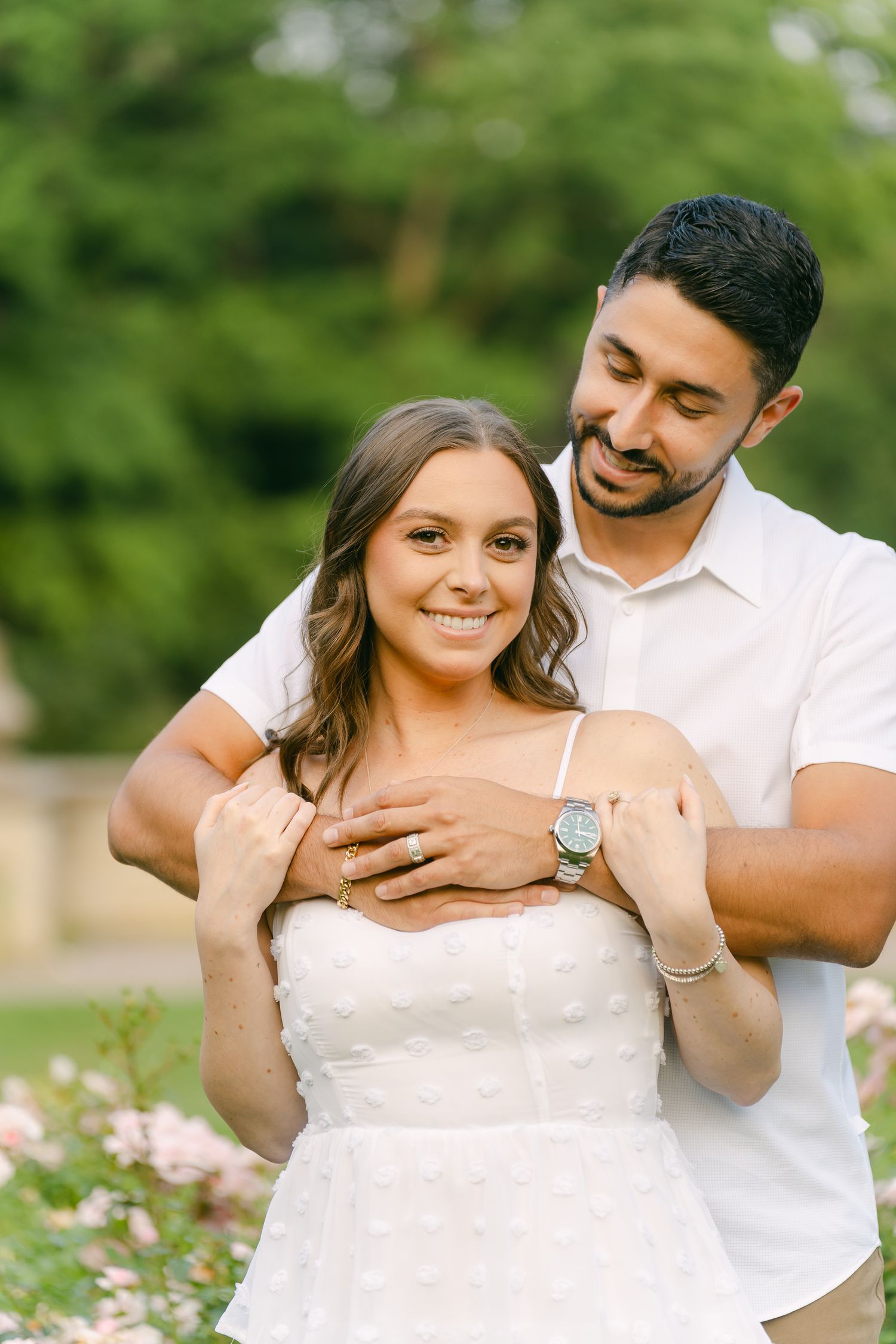 A sunny engagement portrait with a couple sharing a loving moment in a rose garden.