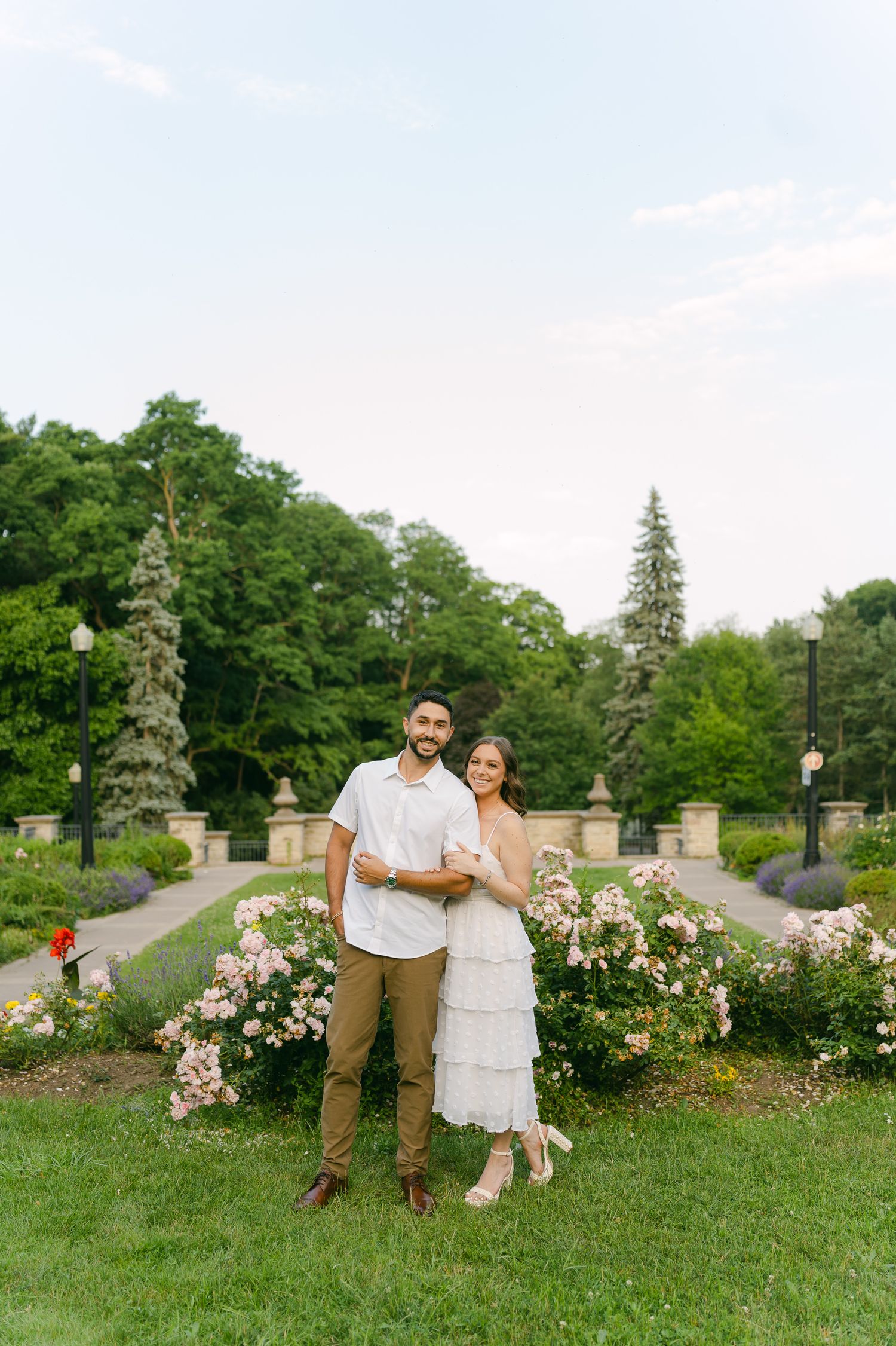 Couple in casual elegant attire poses together in a landscaped garden with stone features.