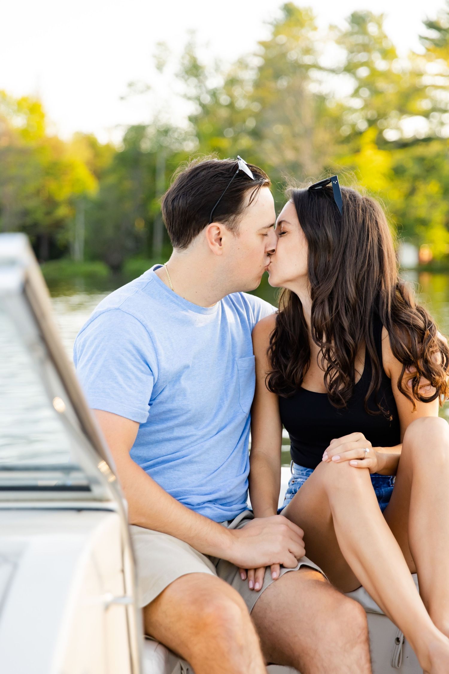 A romantic couple shares a tender kiss while sitting on a boat deck during golden hour.
