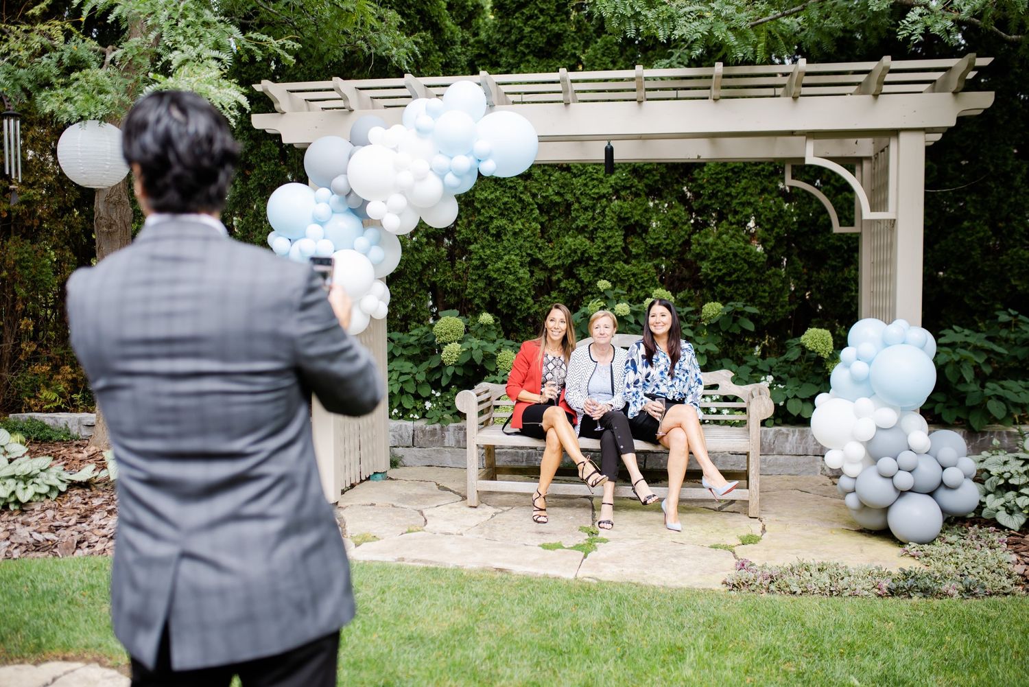 Garden party setup with blue and white balloon arch decorations under a pergola.