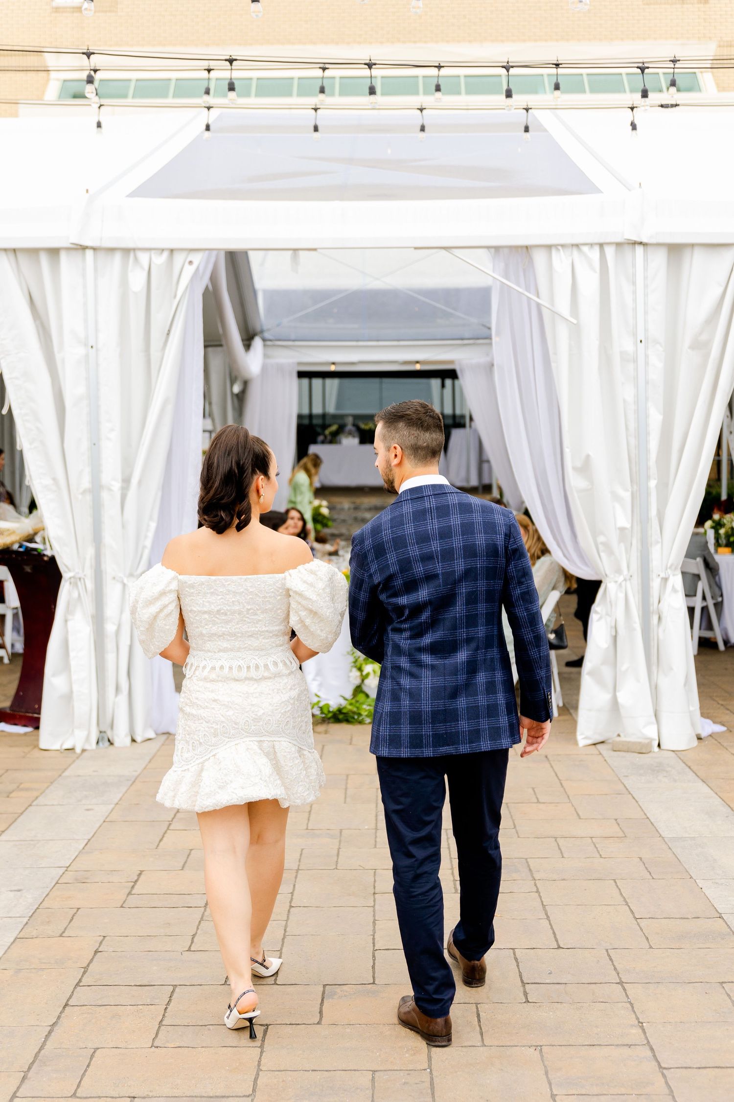 Couple walking through white draped entrance at elegant outdoor event.
