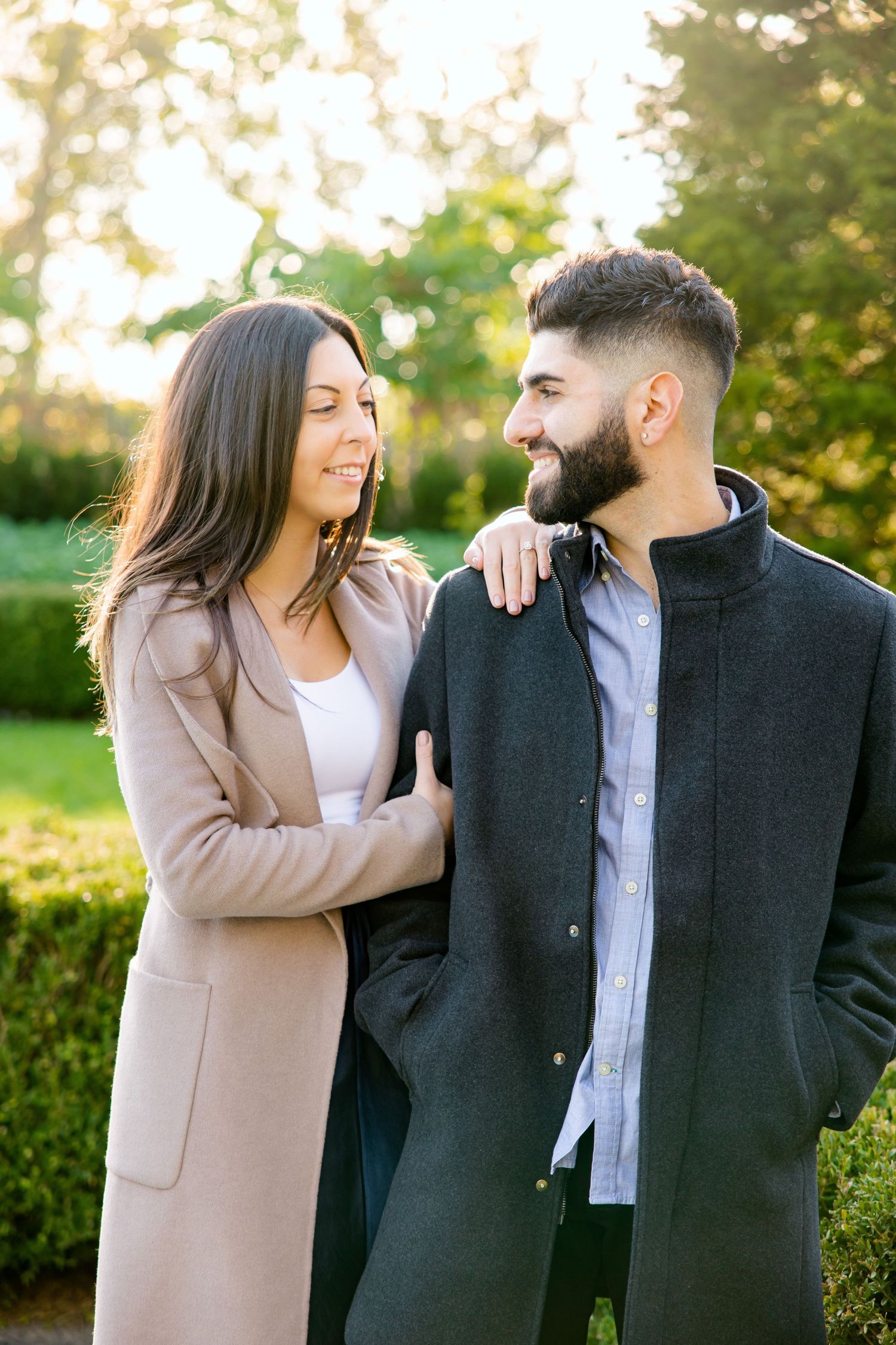 A couple shares an intimate moment while standing in a sun-dappled garden setting.